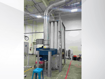 Velký průmyslový ventilační systém, pohled zepředu, s lesklým kovovým potrubím a modrým podstavcem, umístěný v prostorném skladu.