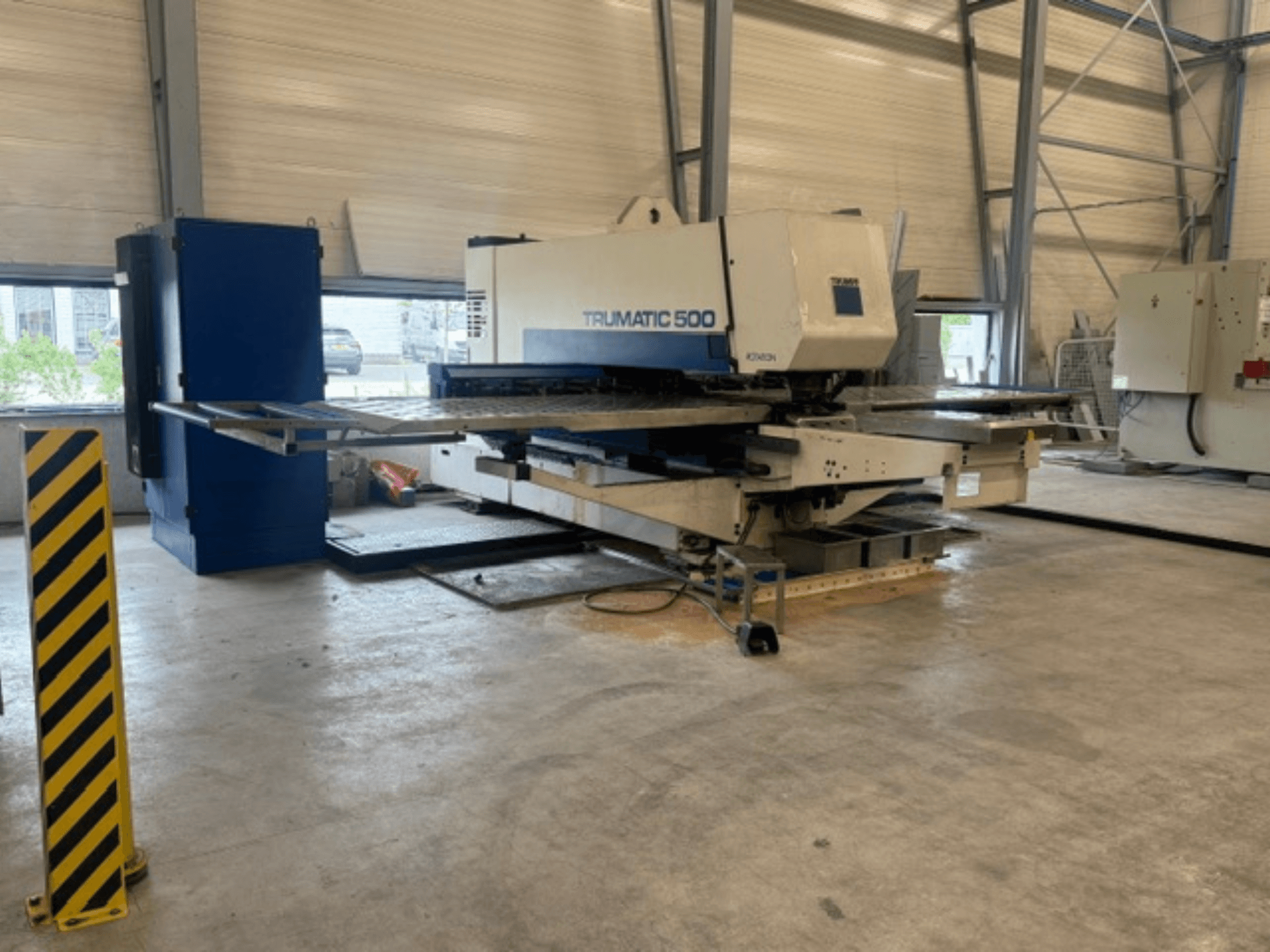 CNC děrovací stroj TRUMPF Trumatic 500 v dílně, boční pohled na stroj a bezpečnostní sloupek se žlutými pruhy.