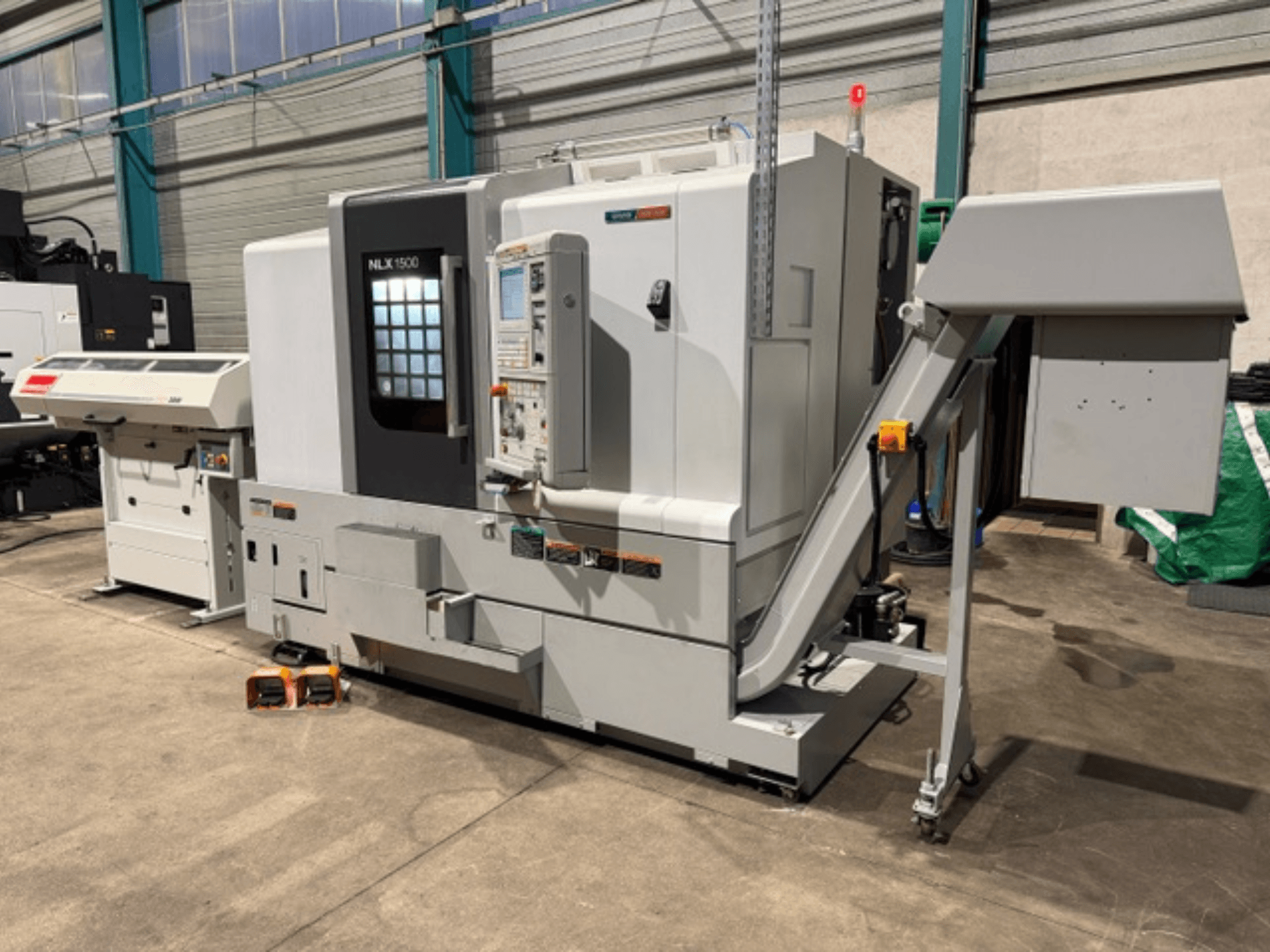 Stroj NLK 1500 CNC, pohled zepředu, s ovládacím panelem a zásobníkem na příslušenství na boku, na betonové podlaze.