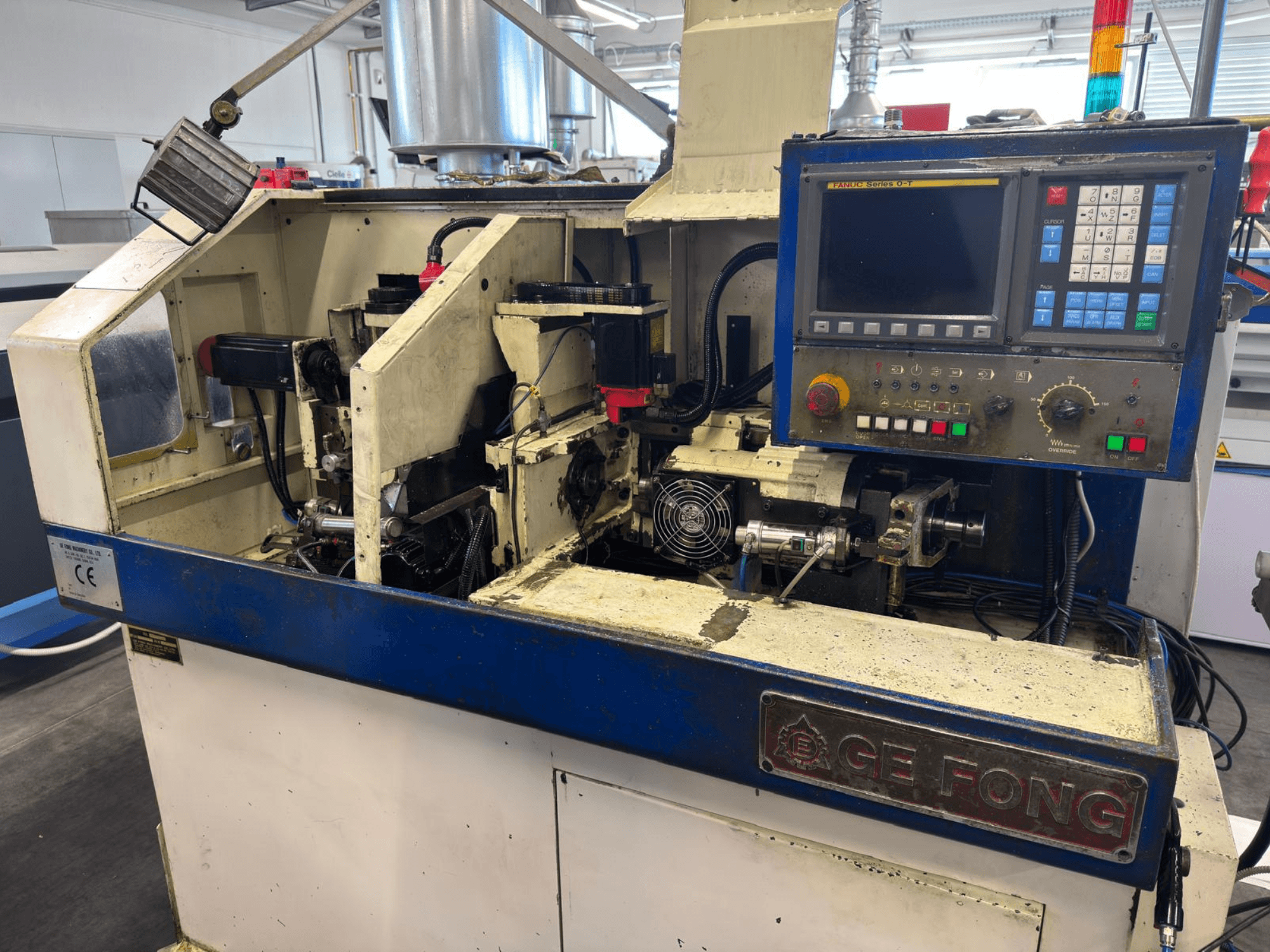 Průmyslový stroj GE FONG v čelním pohledu, zobrazující vnitřní komponenty, ovládací panel a provozní části.