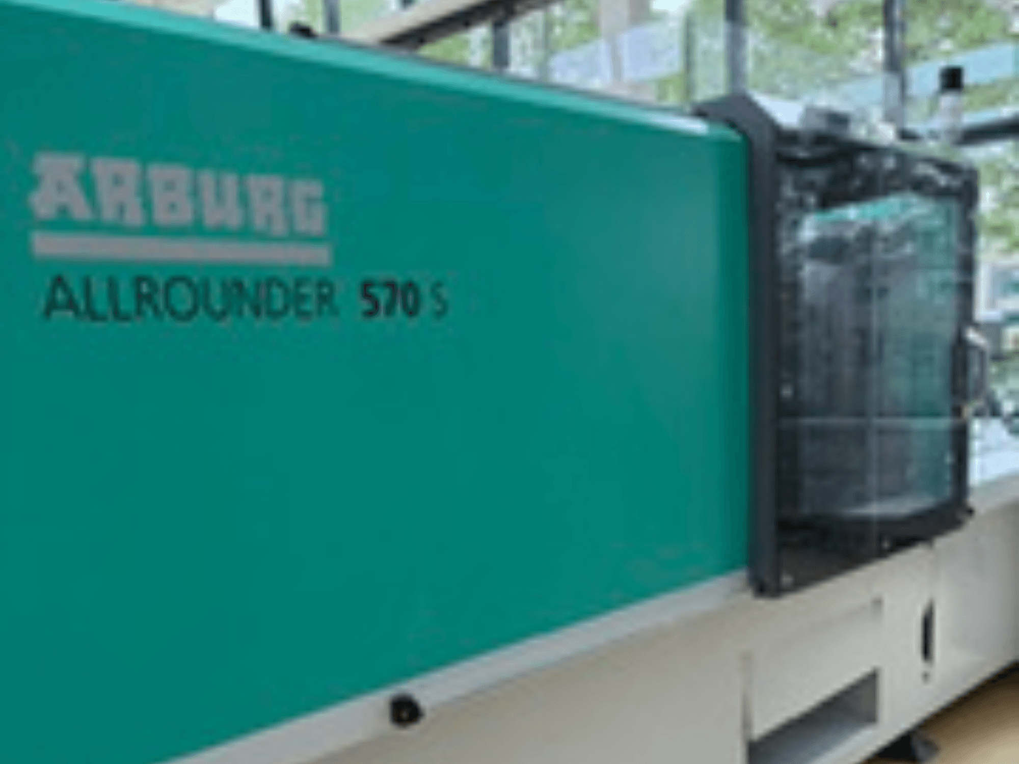 Pohled zepředu na stroj Arburg ALLROUNDER 570 S 1600-290, s vnějším povrchem v barvě teal a vstřikovací jednotkou, který ukazuje část konstrukce stroje.