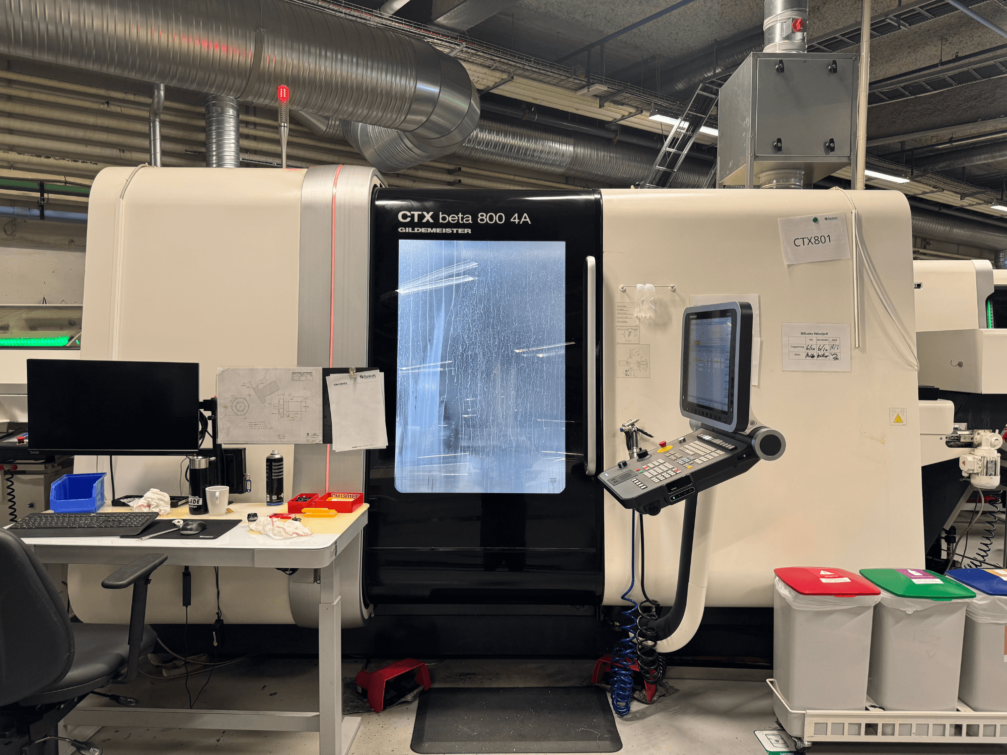 Stroj CTX beta 800 4A s ovládacím panelem a monitorem, boční pohled, v dílně s kancelářskou sestavou a barevnými odpadkovými koši.