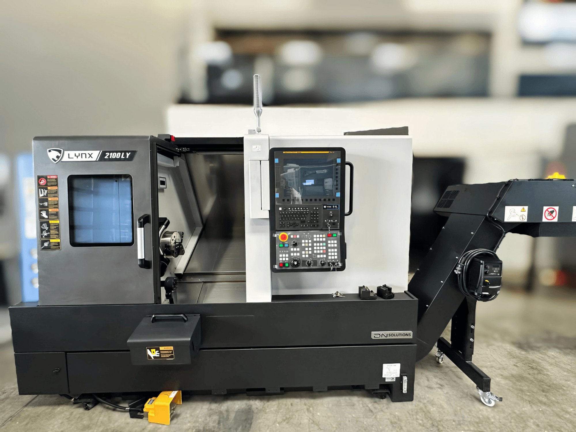 Horizontální soustruh DN SOLUTIONS LYNX 2100LYB, pohled zepředu, s ovládacím panelem a otevřenými dveřmi odhalujícími interiér.