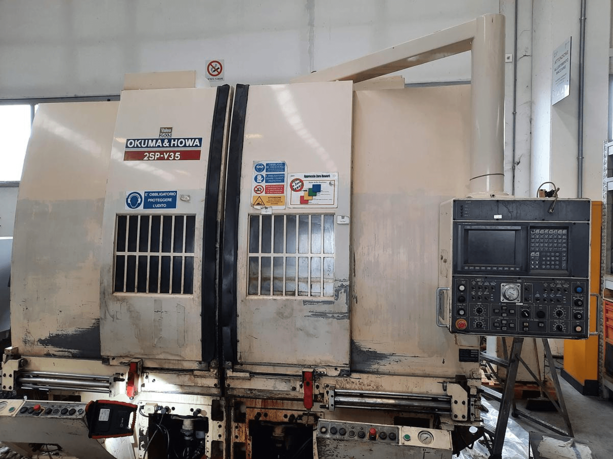 CNC stroj OKUMA & HOWA 2SP-V35 při pohledu zepředu, s ovládacím panelem s různými tlačítky a bezpečnostními štítky.