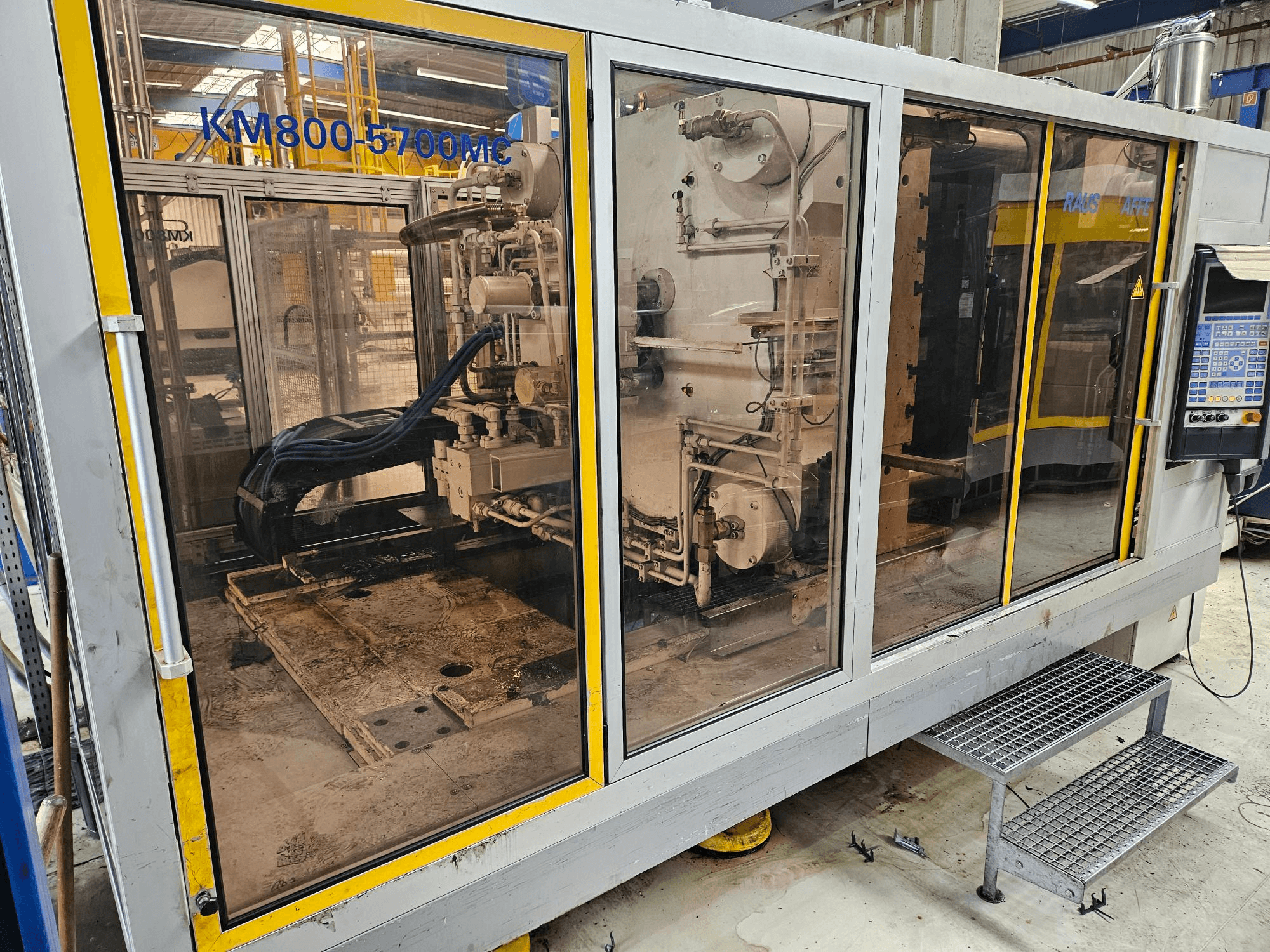 Hydraulický vstřikovací lis Krauss Maffei KM800-5700 MC, pohled zepředu s výhledem na jednotlivé součásti skrz skleněné panely.