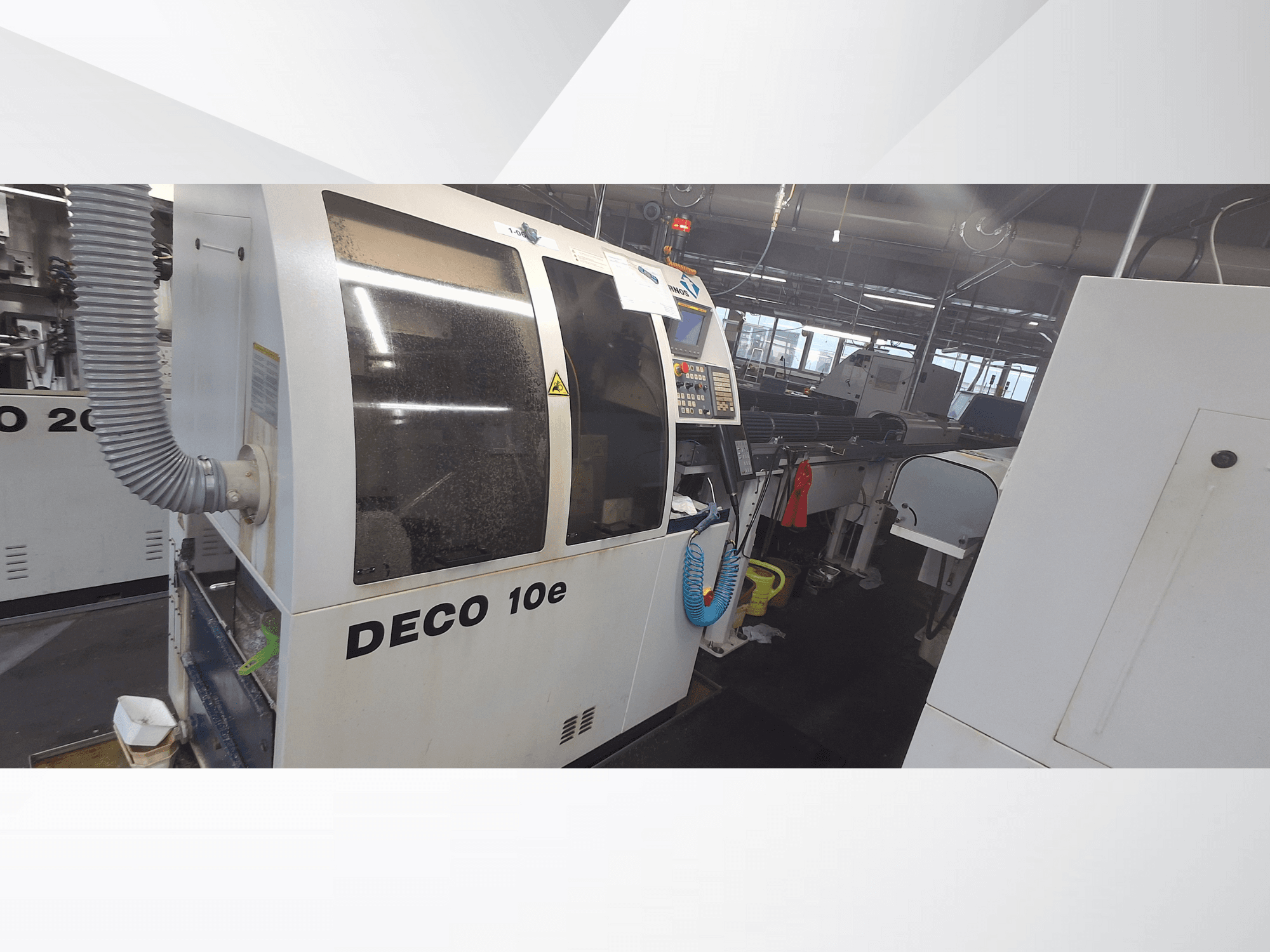 Stroj DECO 10e v dílně; boční pohled na ovládací panel a ventilační hadici, v pozadí rozmazané stroje.