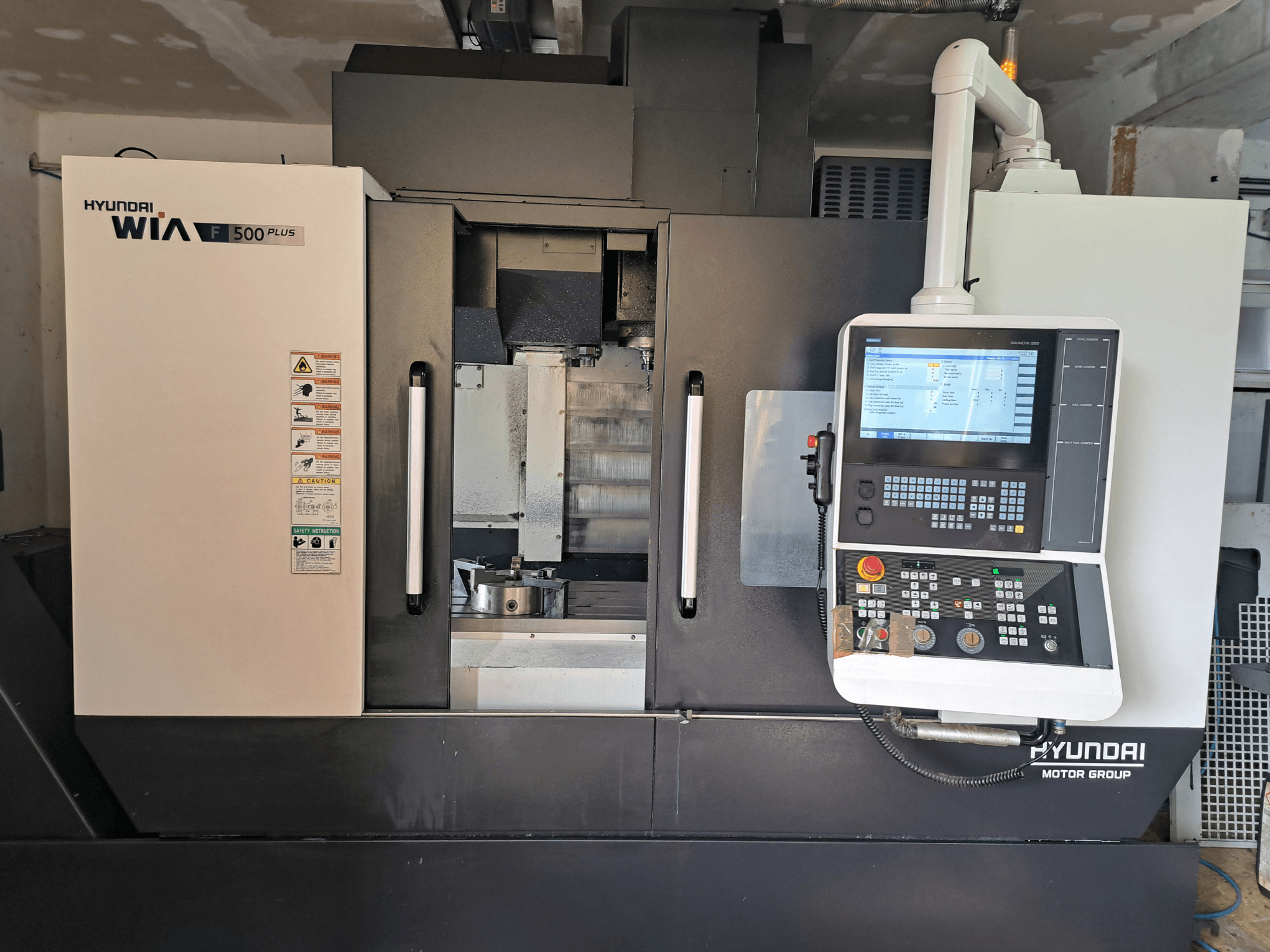 Stroj Hyundai WIA F500 Plus CNC v čelním pohledu, s digitálním ovládacím panelem a bezpečnostními štítky.