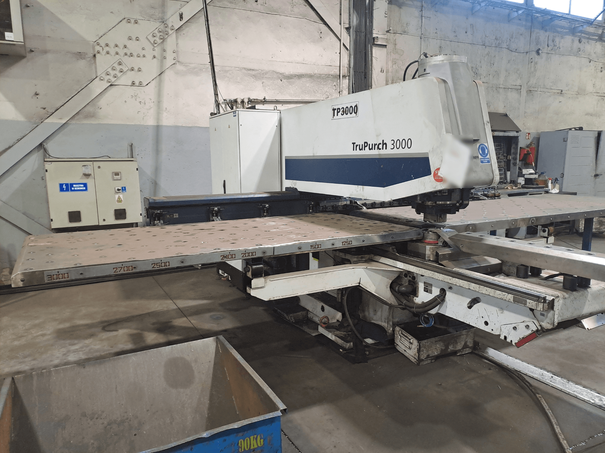 Stroj TruPunch 3000 CNC zobrazený zepředu, s velkou kovovou deskou a měřicími značkami, v průmyslovém prostředí.