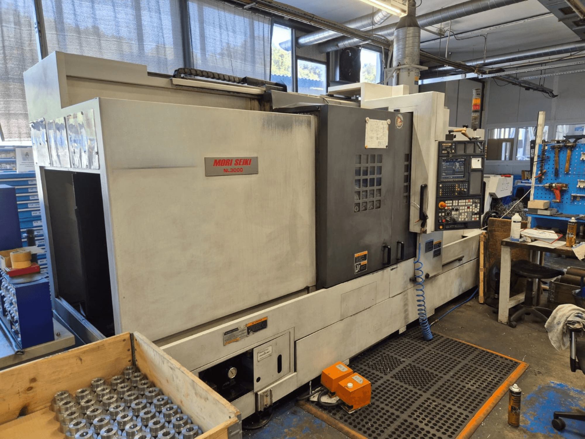 CNC soustruh Mori Seiki NL3000 v dílně, boční pohled na ovládací panel, nástroje a kovové díly v dřevěné skříni.