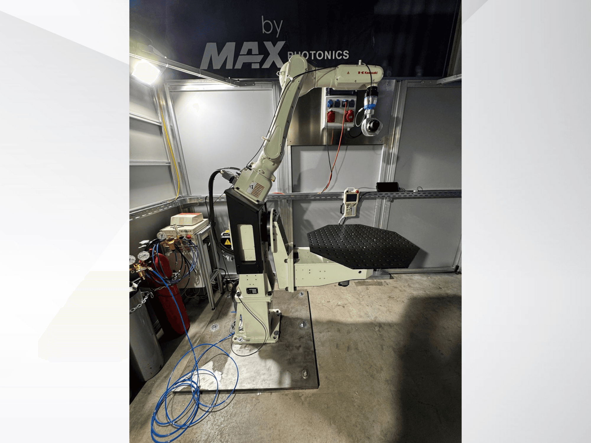 Přístroj s robotickým ramenem Max Photonics, pohled zepředu, s černou perforovanou plošinou a ovládacím panelem s měřidly a kabely.