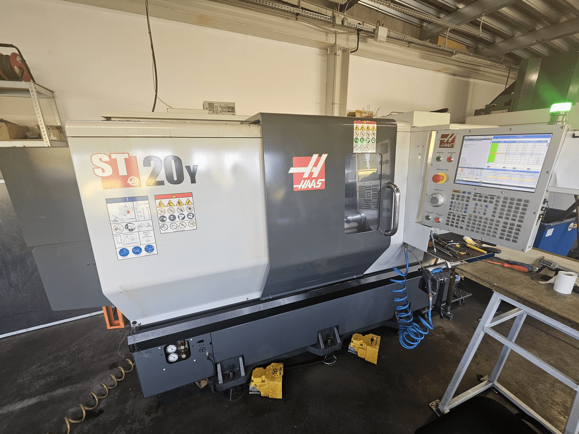 CNC soustruh Haas ST-20Y v čelním pohledu s ovládacím panelem; včetně bezpečnostních štítků a detailu vzduchové hadice na boku.