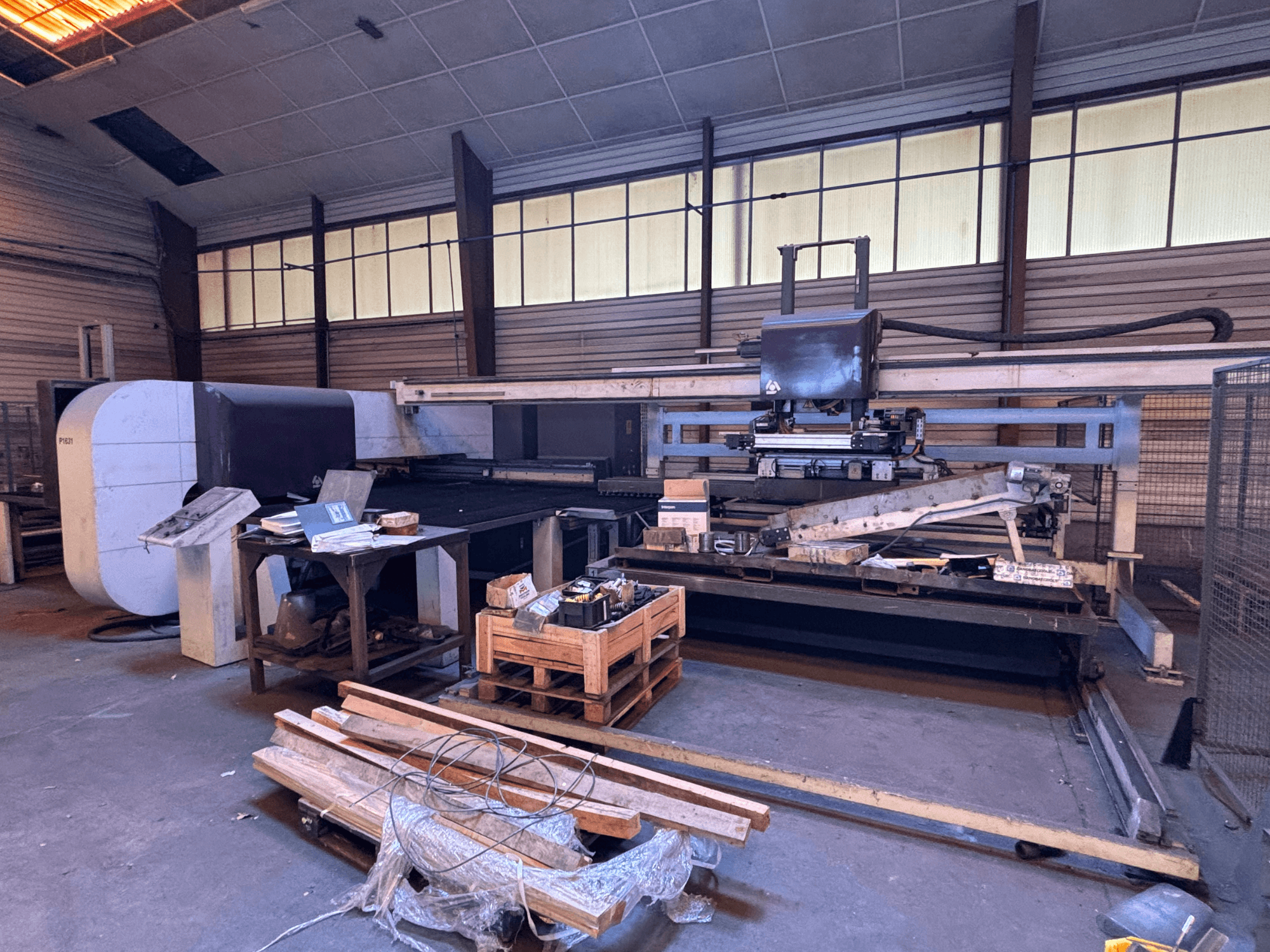 CNC děrovací stroj DANOBAT P1631 v dílně, pohled zepředu, obklopený materiálem a nástroji na přeplněné podlaze.