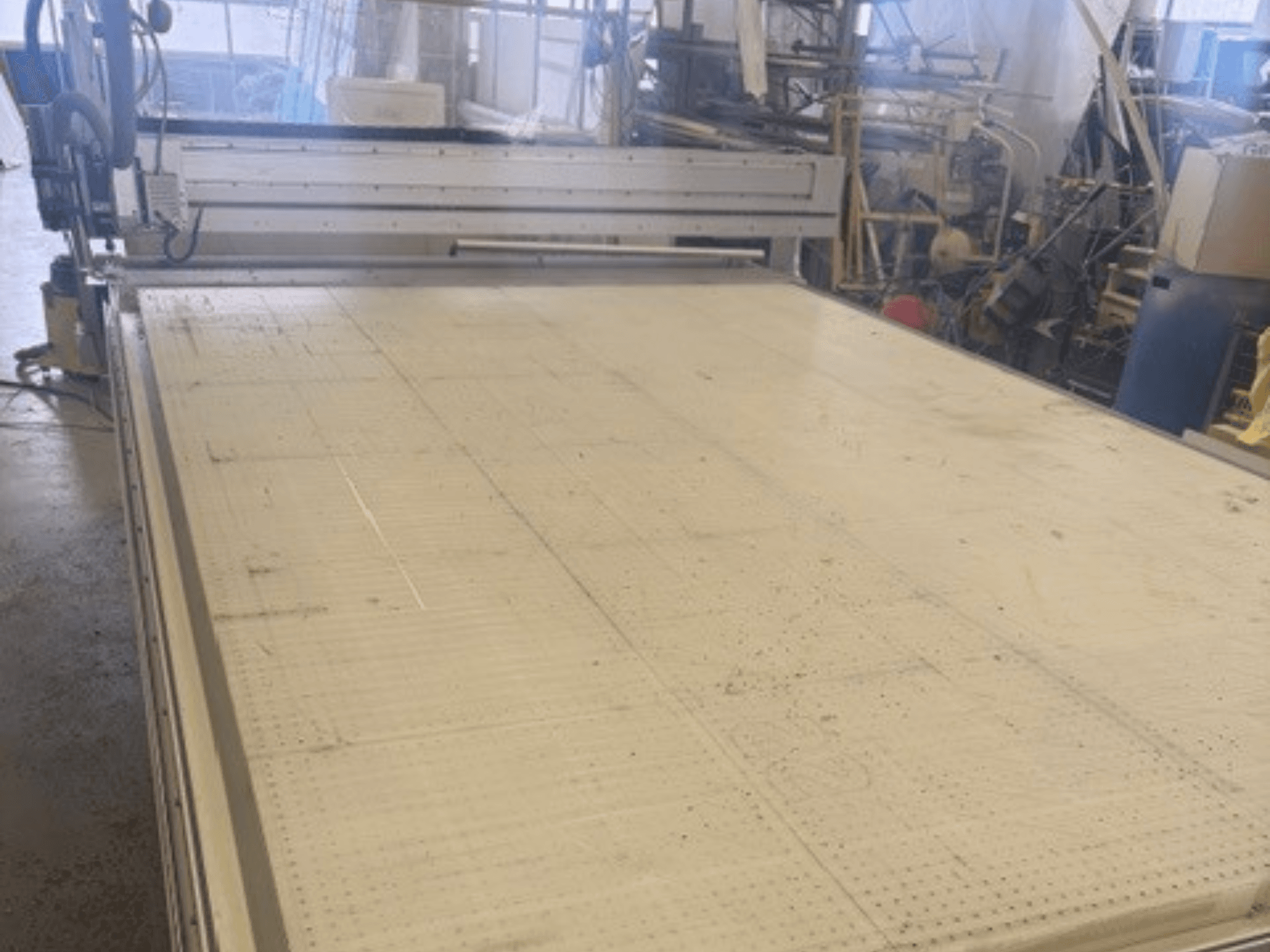 Velký řezací stroj s rovným povrchem, na kterém je vidět rám a vodicí lišta; pohled z úhlu v dílně.