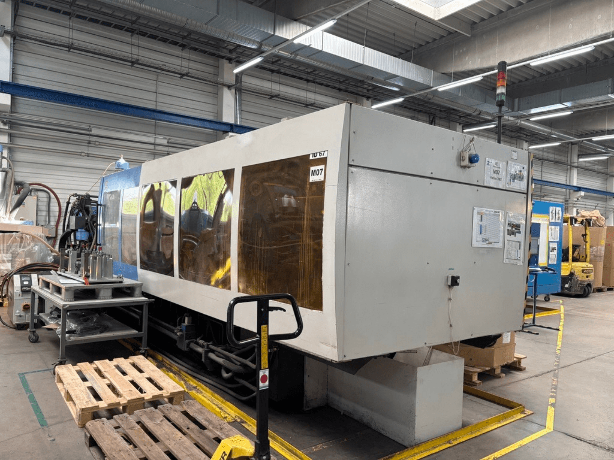Hydraulický vstřikovací lis HAITIAN 7000/5000 v továrně, boční pohled s viditelnými ovládacími panely a bezpečnostními světly.