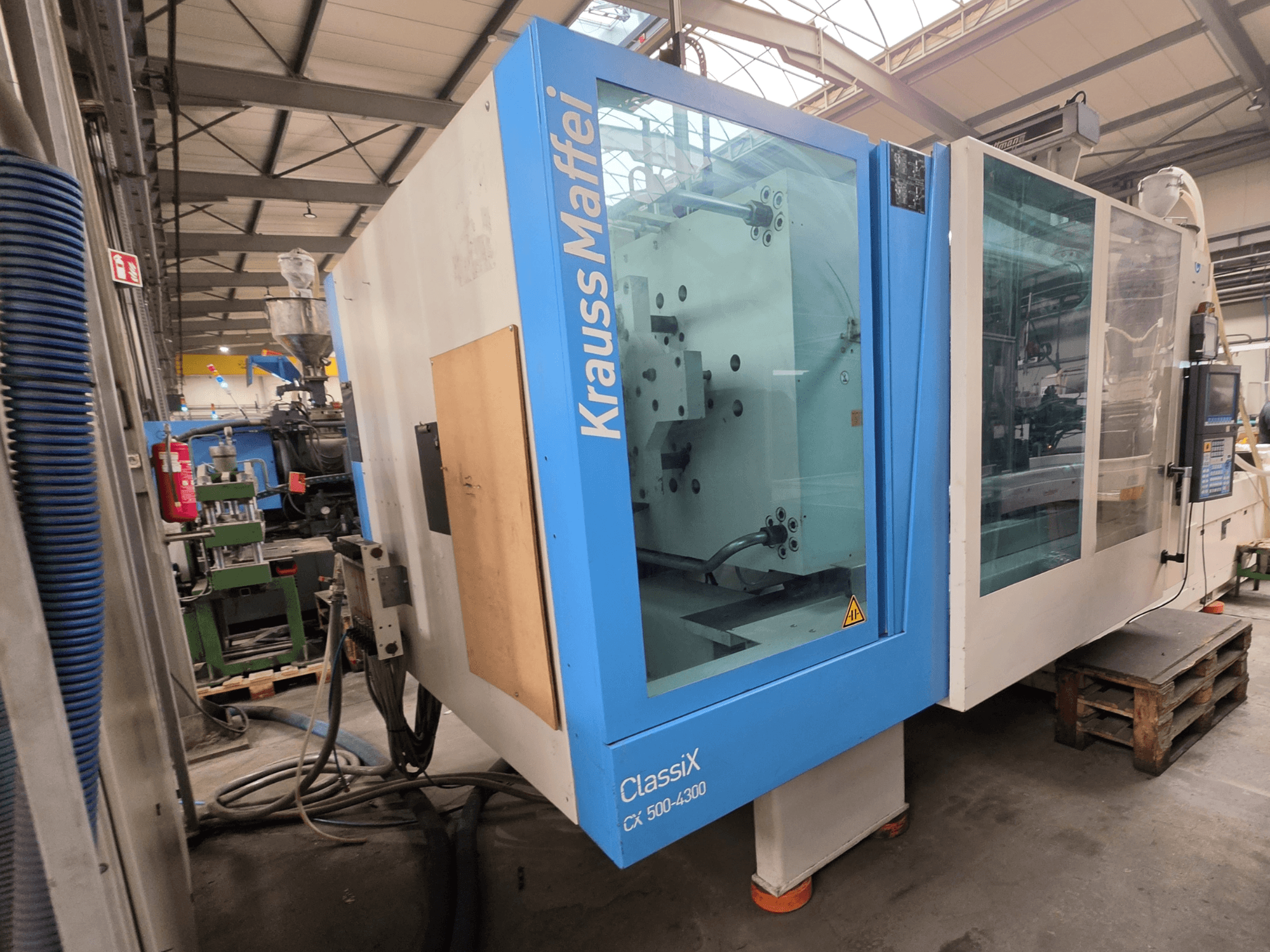 Hydraulický vstřikovací stroj Krauss Maffei 500-4300 CX, boční pohled na ovládací panel a provozní komponenty.