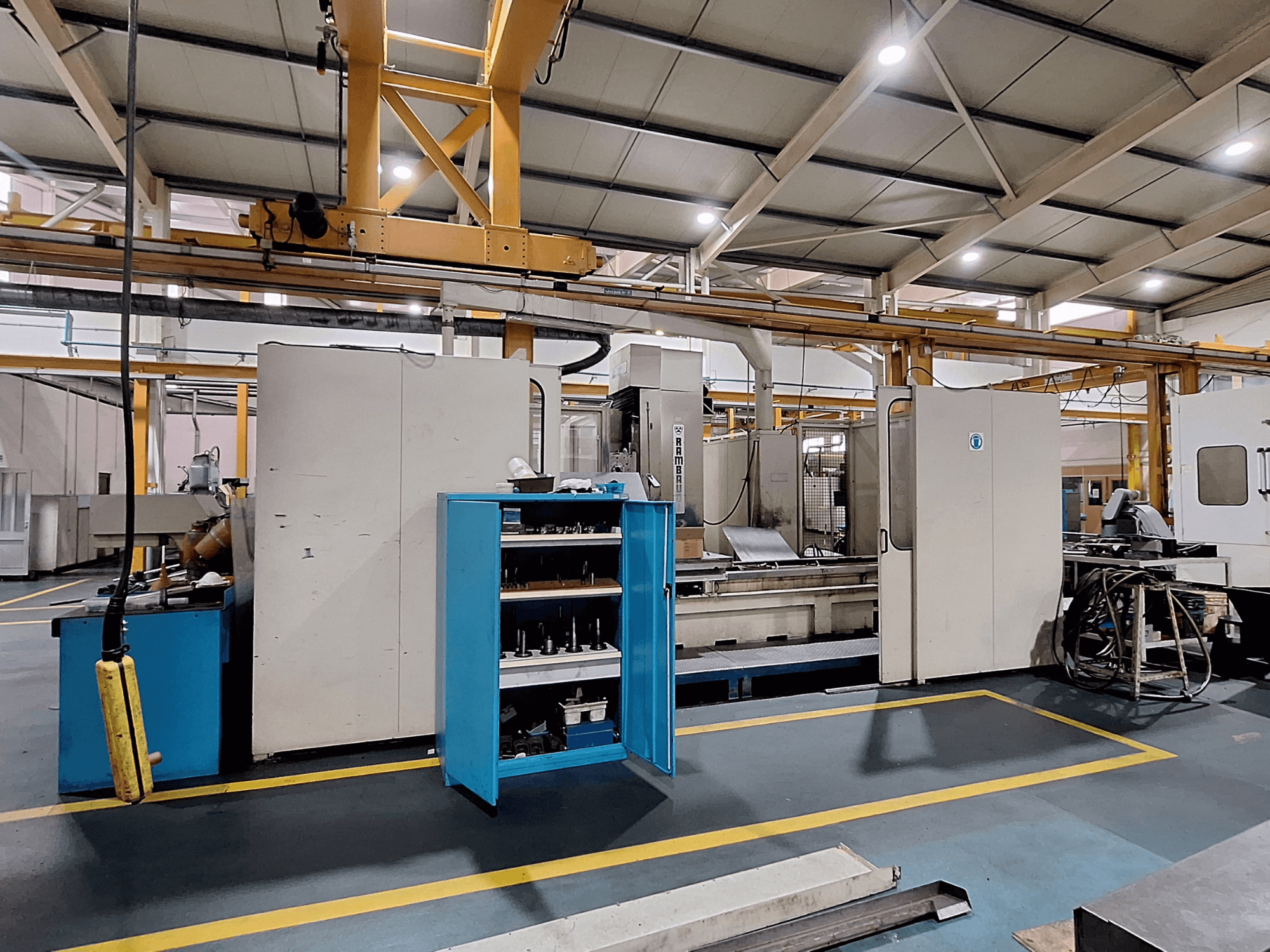 Portálová frézka Rambaudi RX 1250, pohled zepředu s úložným prostorem pro nástroje, v prostorném průmyslovém pracovním prostoru.