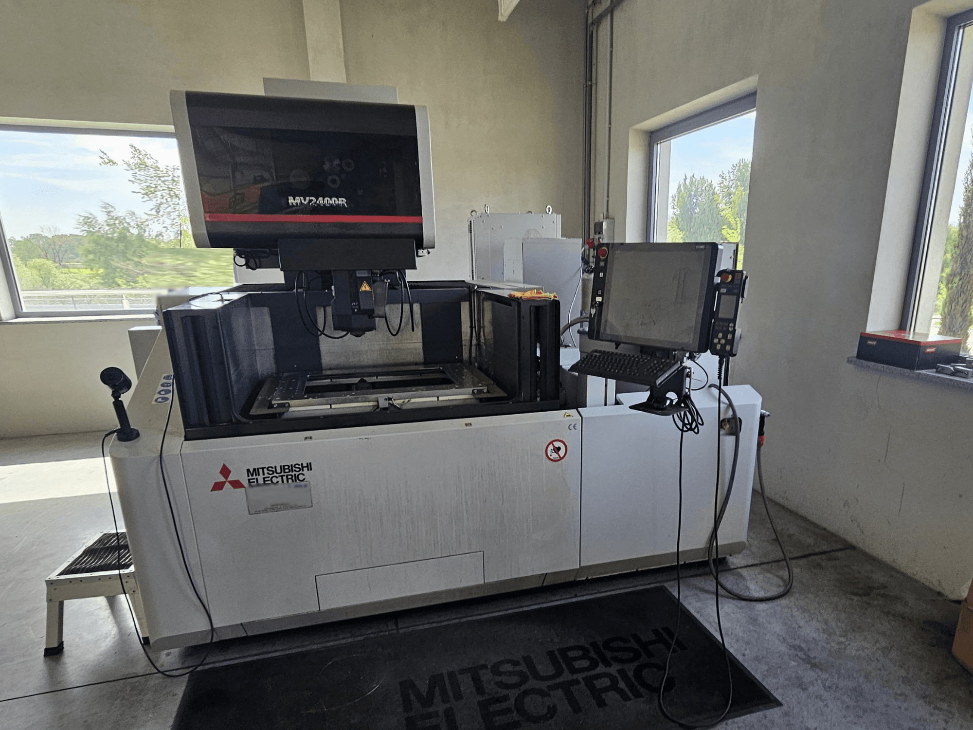 Drátový elektroerozivní stroj Mitsubishi MV2400R v dílně s dotykovým ovládacím panelem a pracovním prostorem.