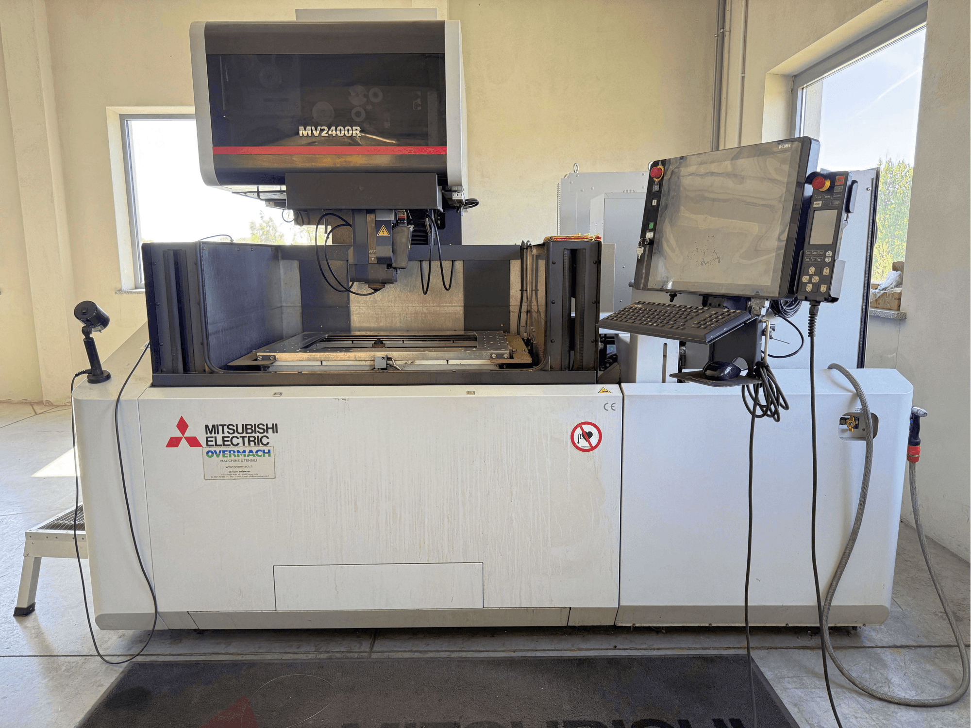 Elektroerozivní stroj Mitsubishi MV2400R v čelním pohledu, na kterém je vidět ovládací panel, pracovní prostor a bezpečnostní značení.
