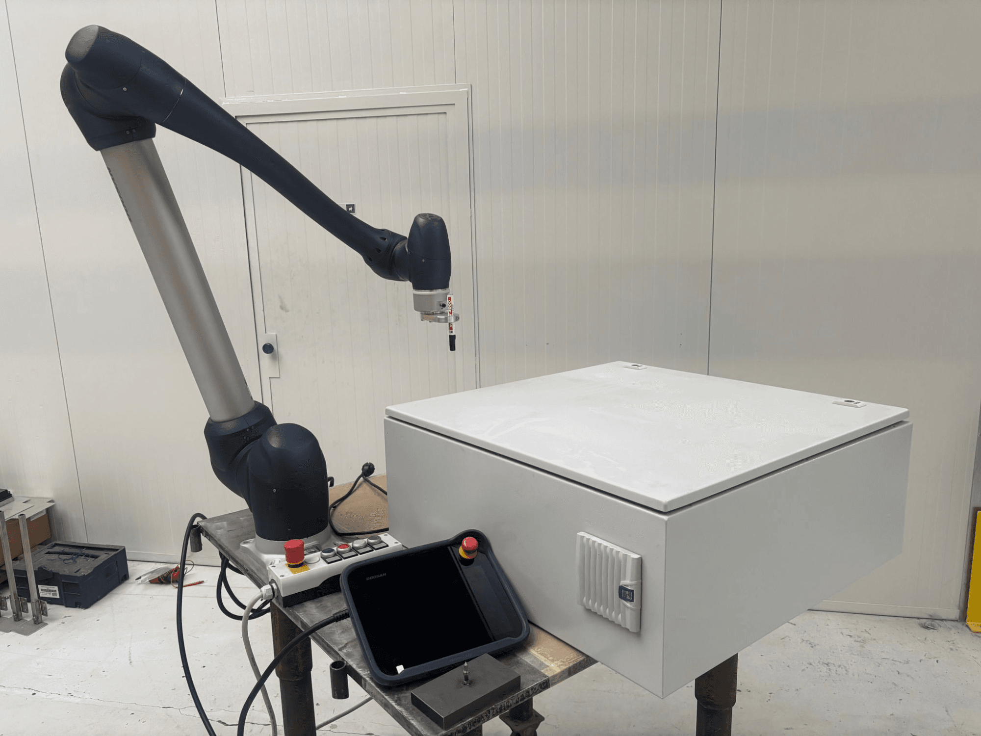 Kolaborativní robot DOOSAN M0617 v bočním pohledu s nataženou robotickou rukou nad ovládacím rozhraním a bílou krabicí na stole.