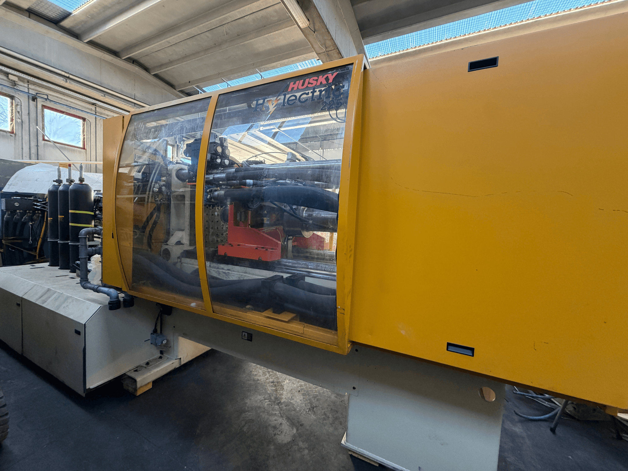 Elektrický vstřikovací stroj Husky HL225 RS65, pohled zepředu se žlutým krytem, viditelným ovládacím panelem a hydraulickými komponenty.