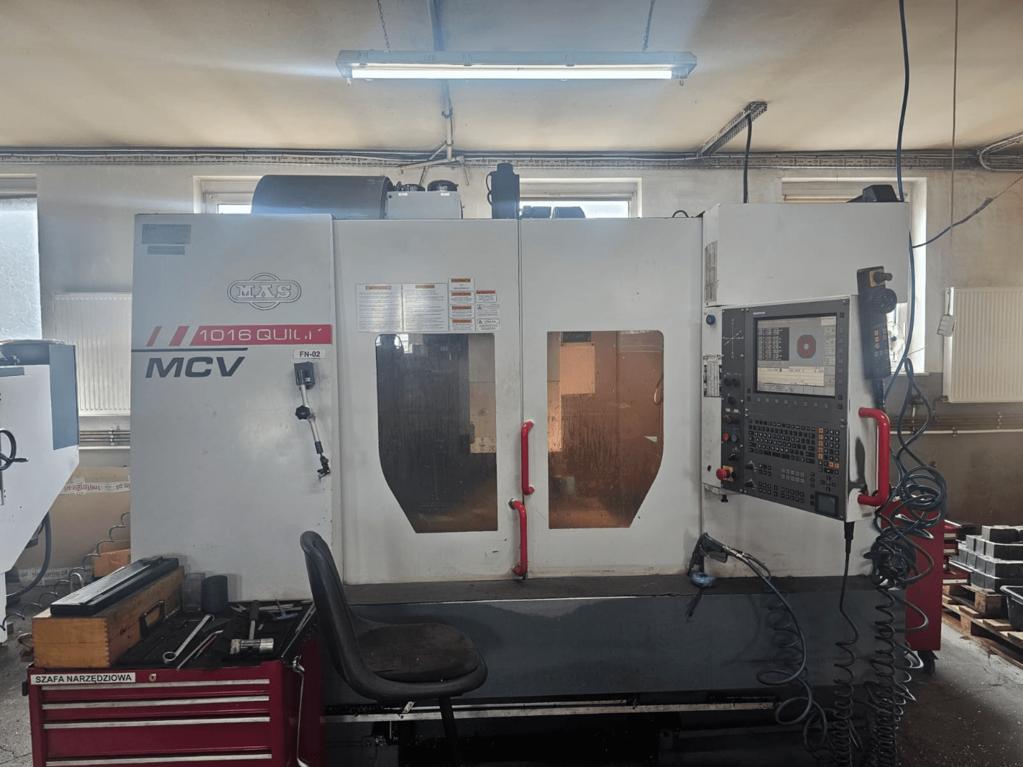 Stroj MVS MCV 1016 QUILL CNC, pohled zepředu, s ovládacím panelem, zásuvkou na nástroje a pracovním prostorem s nástroji.