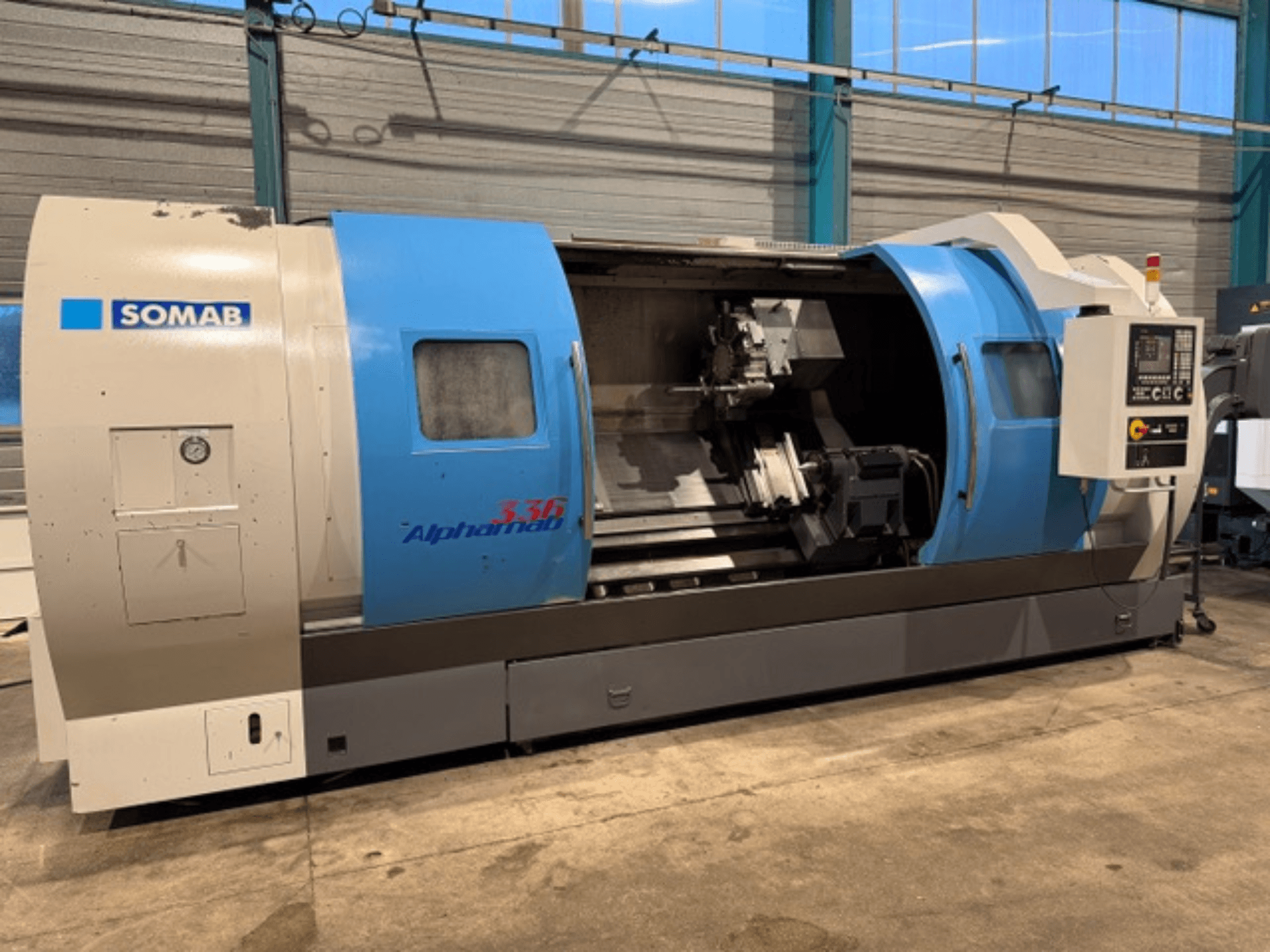 Soustruh SOMAB Alpha 336 CNC, pohled zepředu, s modrošedým krytem a ovládacím panelem na boku pro obsluhu.