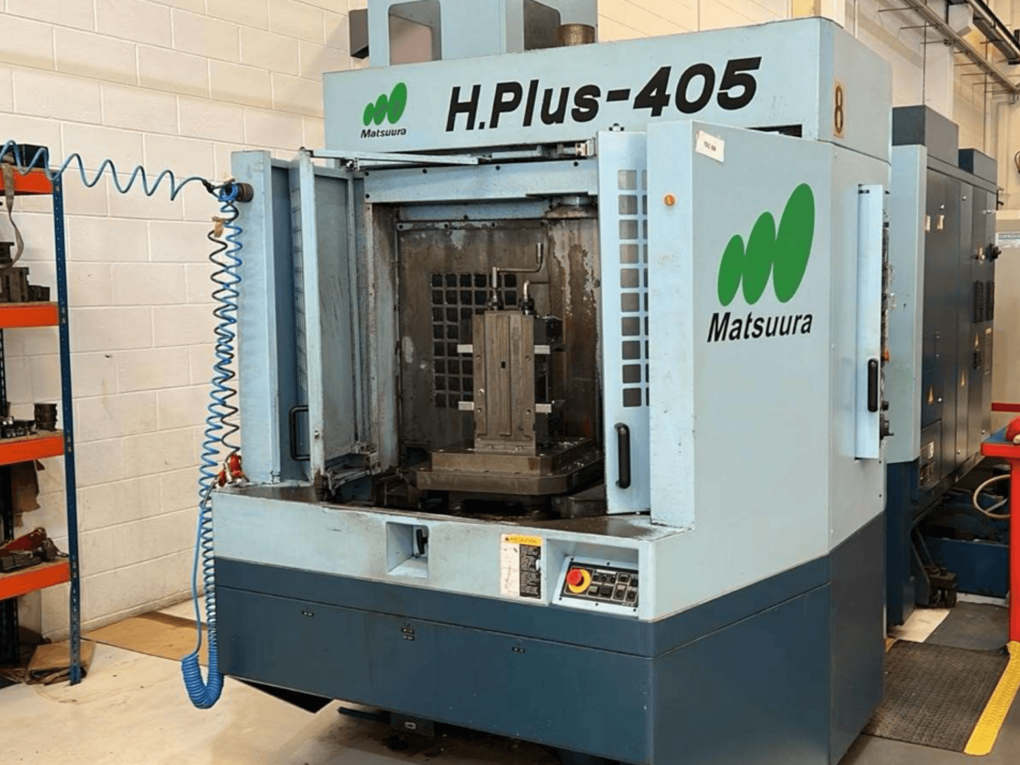 Pohled zepředu na horizontální obráběcí centrum Matsuura H.Plus 405 s otevřenými dvířky, na kterém je vidět pracovní prostor a ovládací panel.