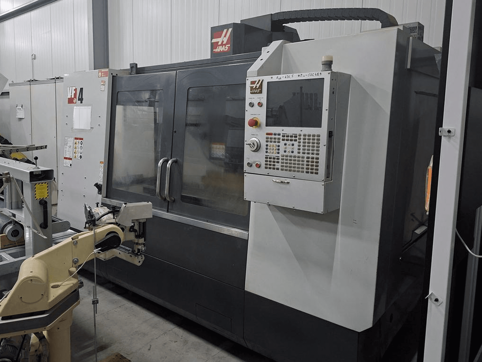 CNC frézka Haas VF-4 v čelním pohledu, vybavená numerickým řídicím panelem a robotickým ramenem pro automatizaci.