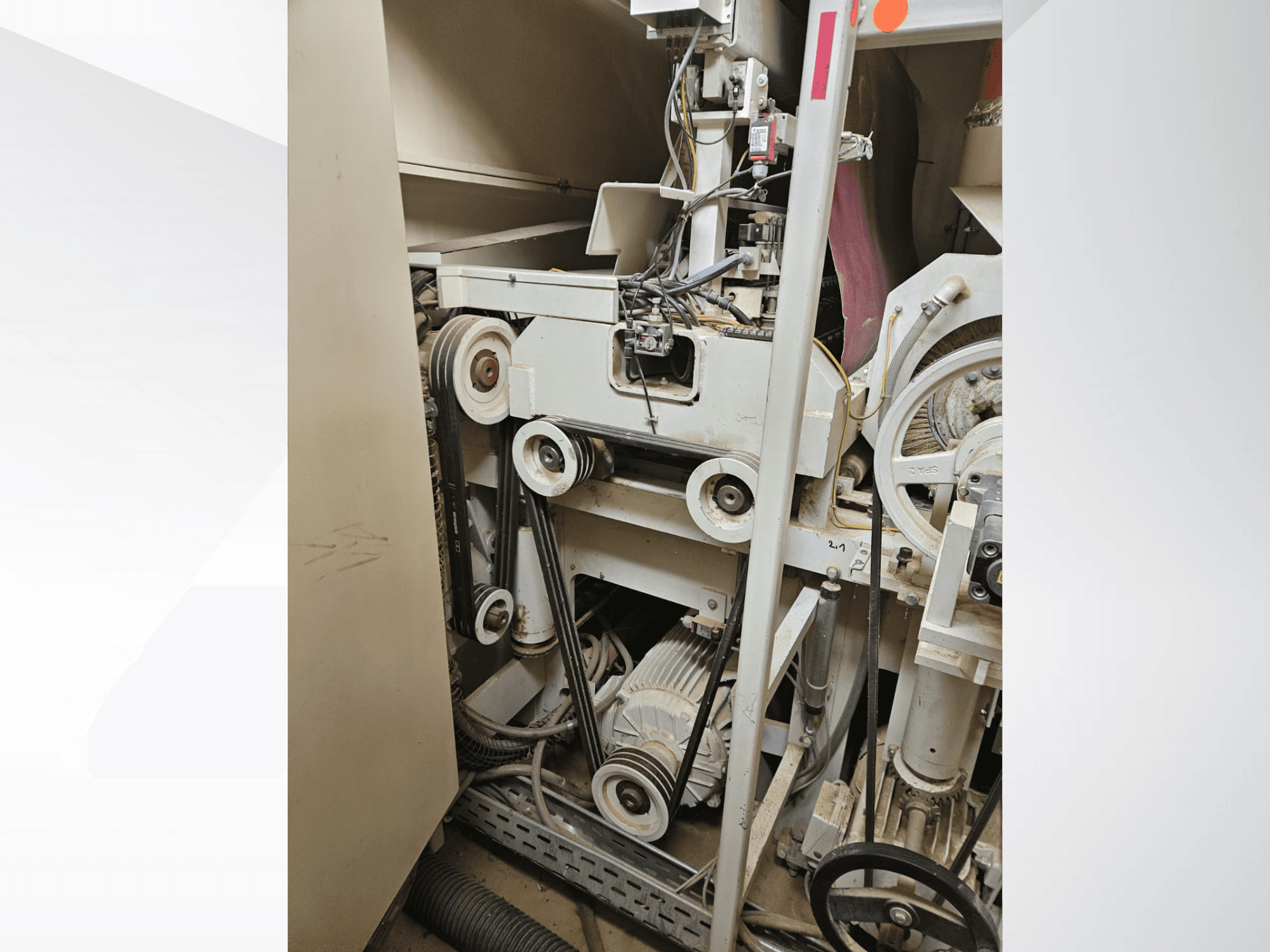 Interiér průmyslového stroje s řemeny a řemenicemi, s motorem a elektroinstalací, pohled z boku.