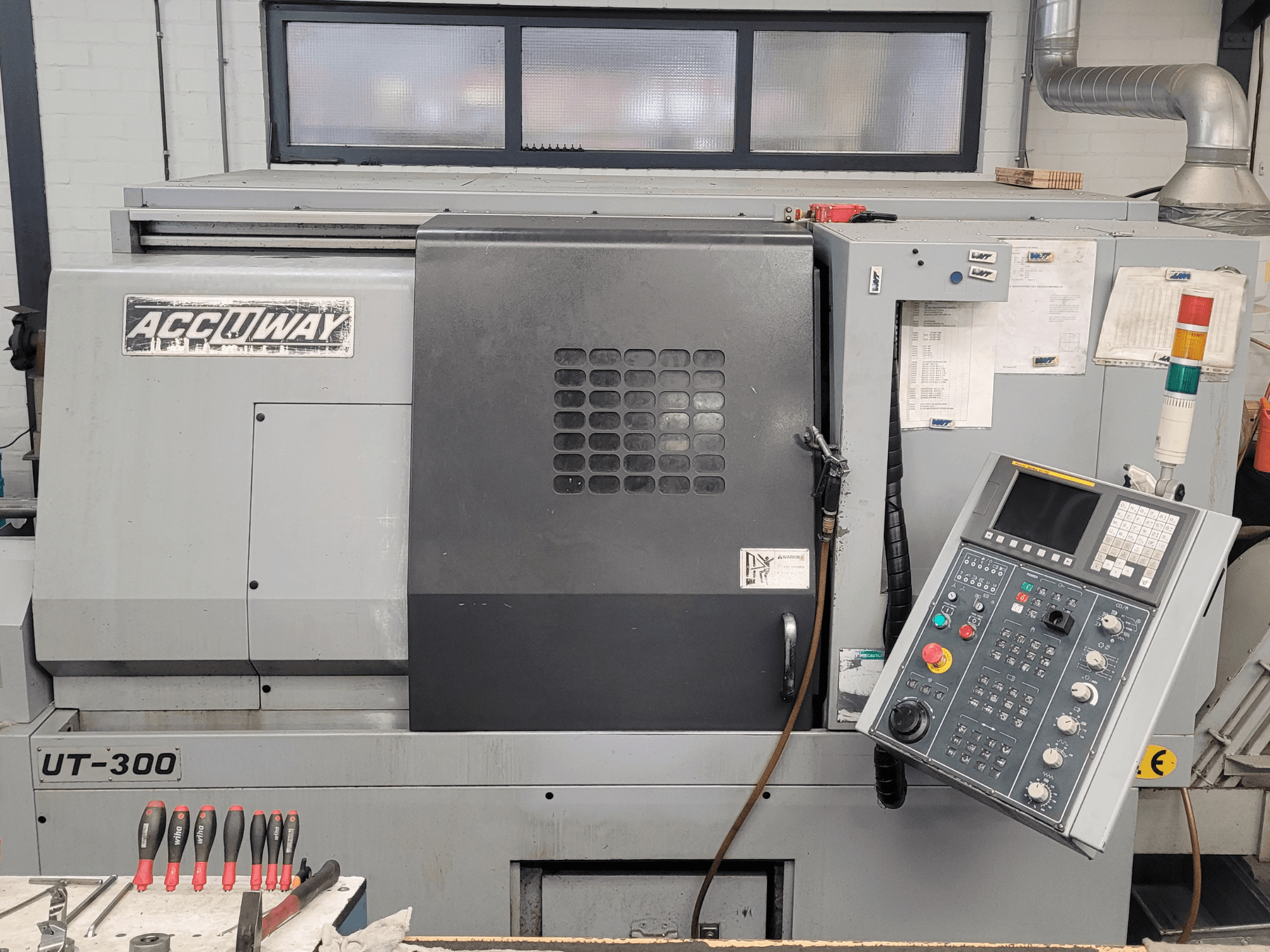 CNC stroj Accuway UT-300 z čelního pohledu, s ovládacím panelem a různými ovládacími tlačítky, v dílenském prostředí.