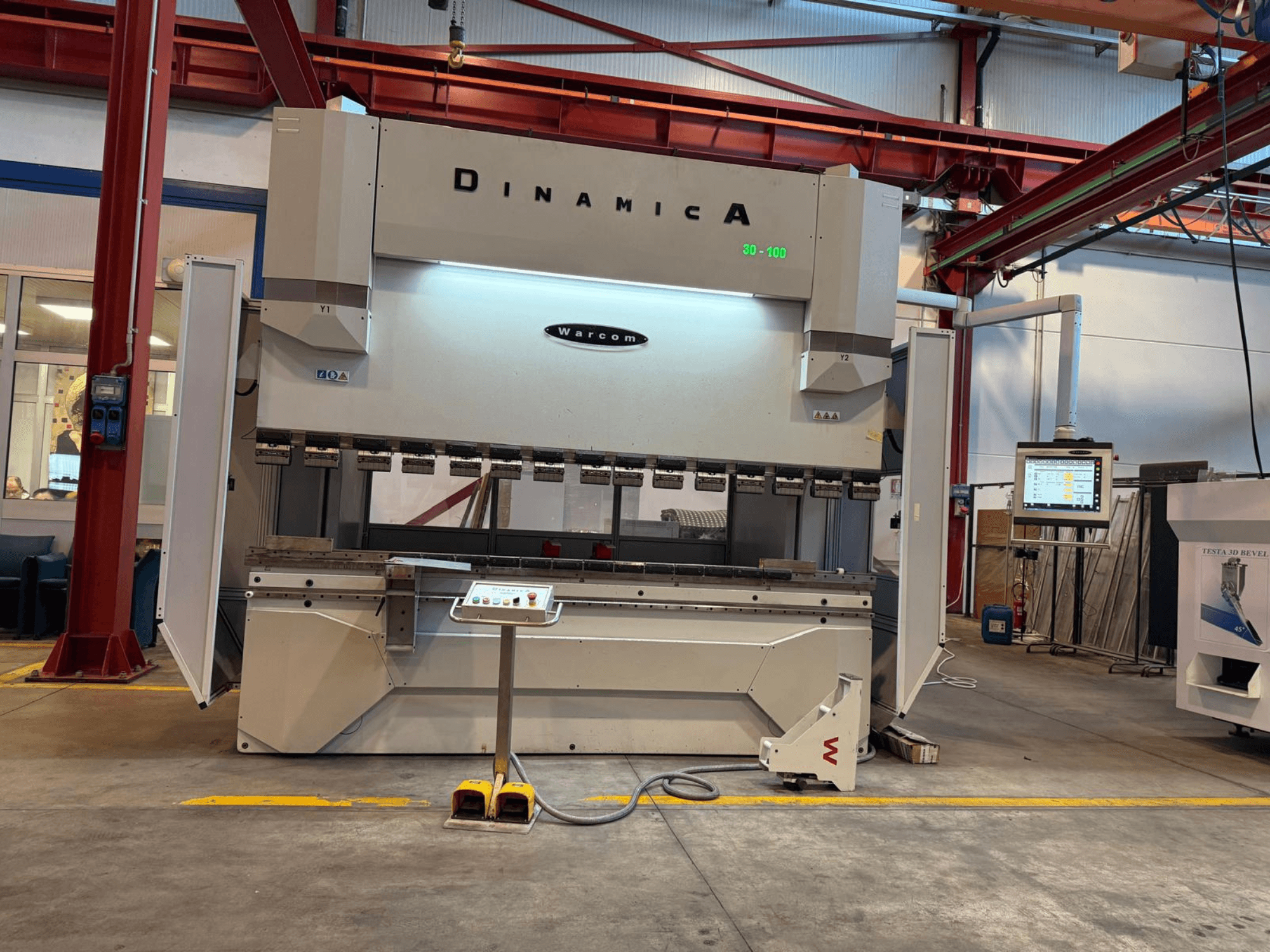 Hydraulická lisovací brzda Dinamica Warcom, pohled zepředu. Obsahuje ovládací panel a několik nástrojových stanic pro přesné ohýbání.