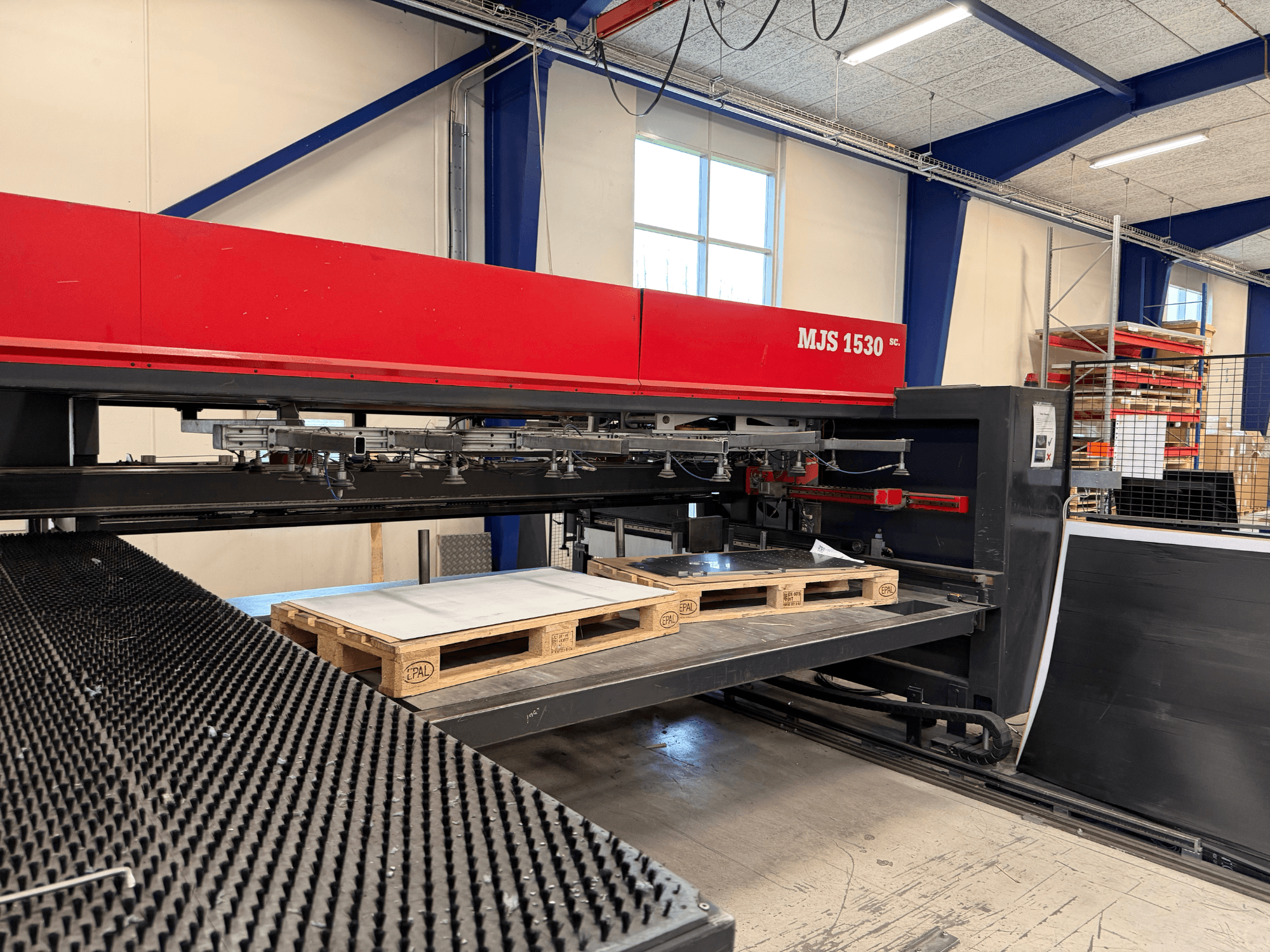 Stroj MJS 1530 CNC v dílně, pohled zepředu, s dřevěnou paletou držící plech na vyvýšené plošině.