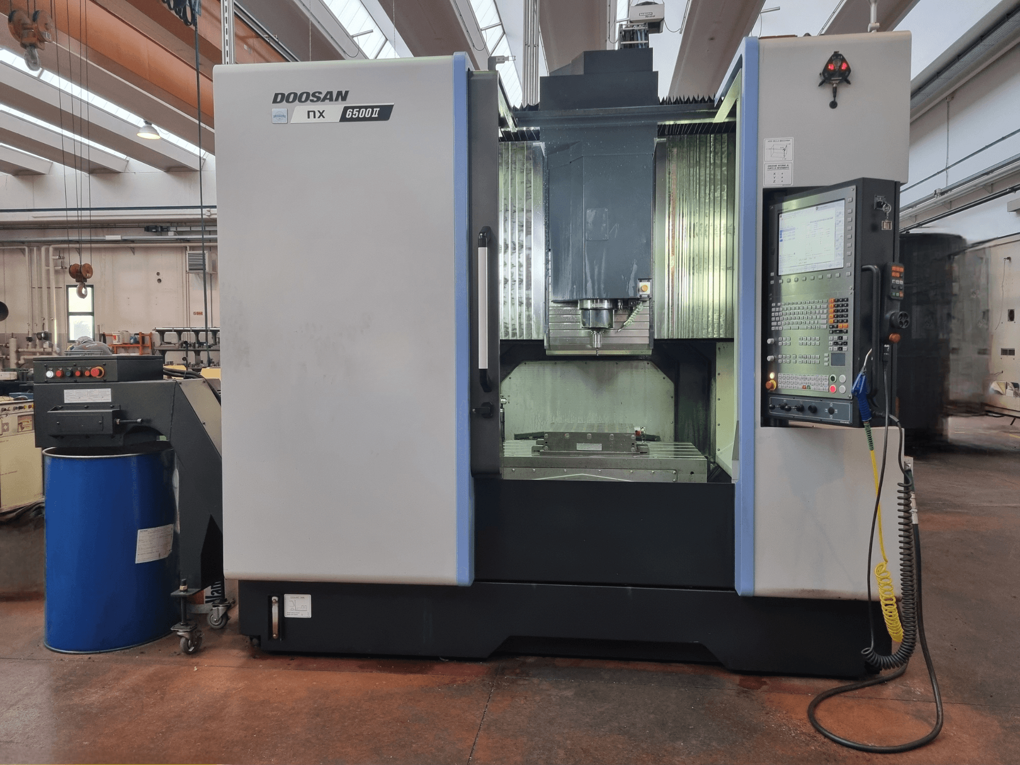 Stroj Doosan NX 6500 II CNC, pohled zepředu, s ovládacím panelem a obráběcím prostorem, umístěným vedle modrého válce.