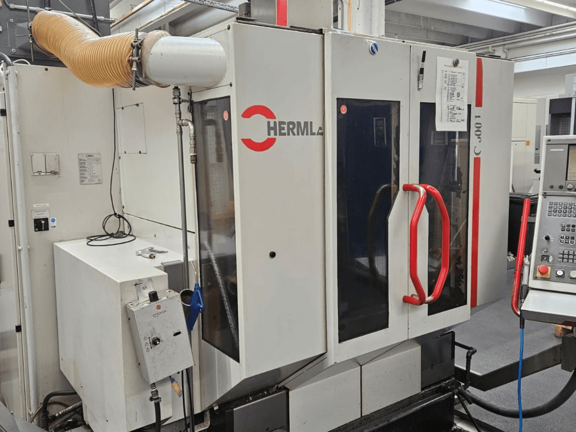 Pohled zepředu na univerzální obráběcí centrum HERMLE C 600 U, zobrazující ovládací panel a červené úchyty na dveřích.