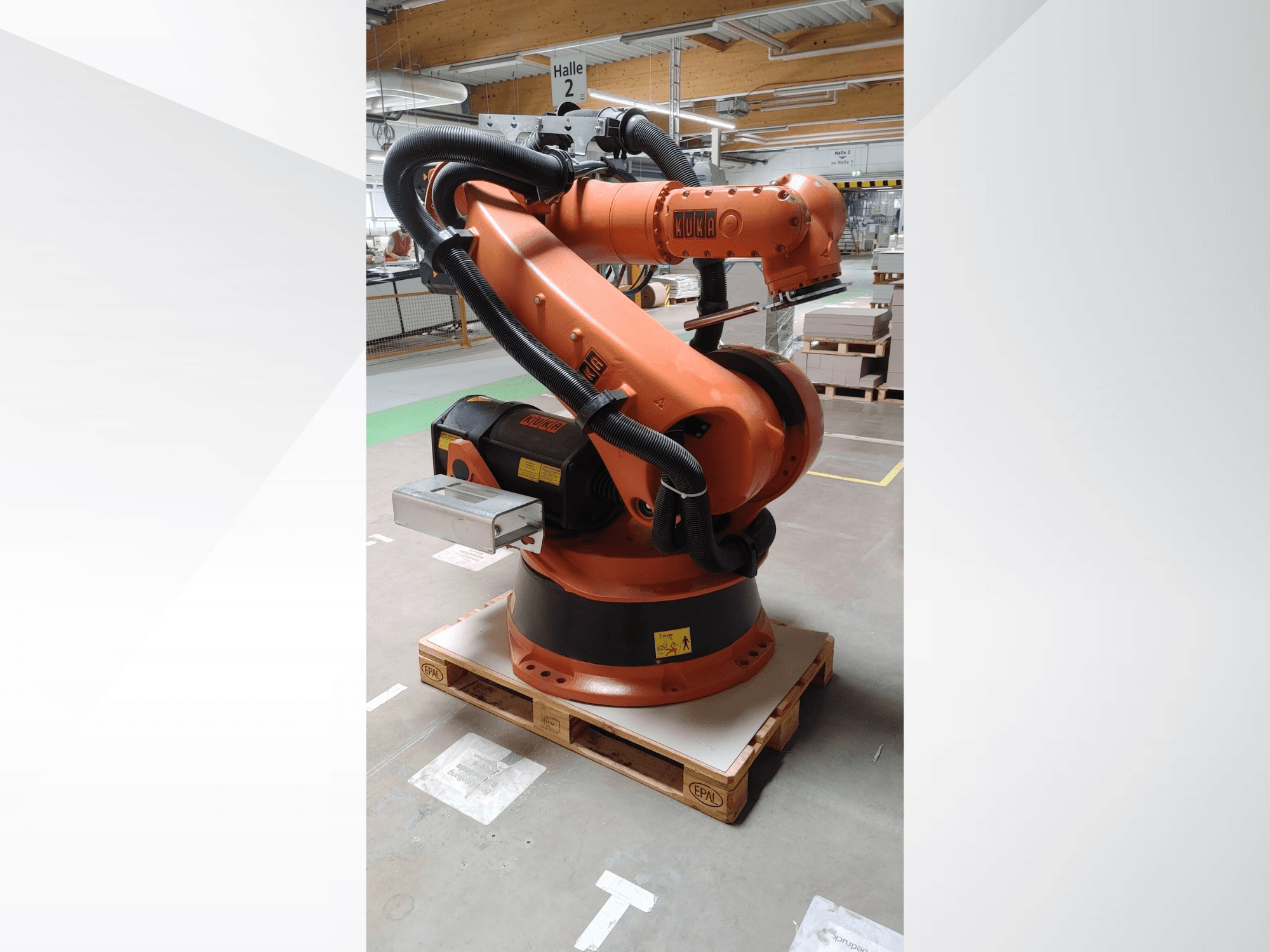 Robotické rameno KUKA KR140-3 COMP v oranžové barvě, pohled zepředu na dřevěné paletě, se zakřiveným ramenem a ovládacím boxem.