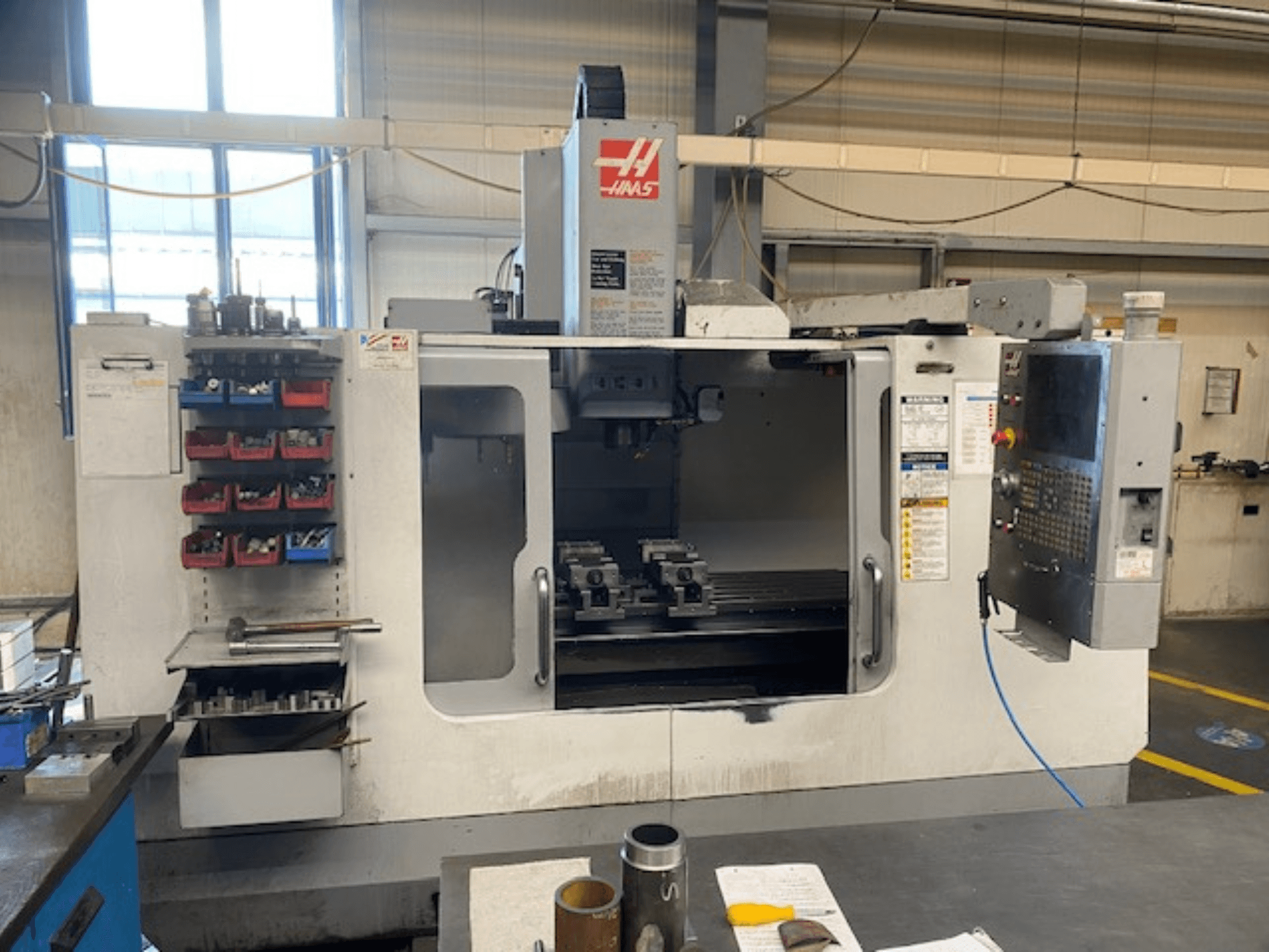 Pohled zepředu na CNC frézku Haas, model VF-2, s viditelným úložným prostorem pro nástroje, ovládacím panelem a nástroji v pracovním prostoru.