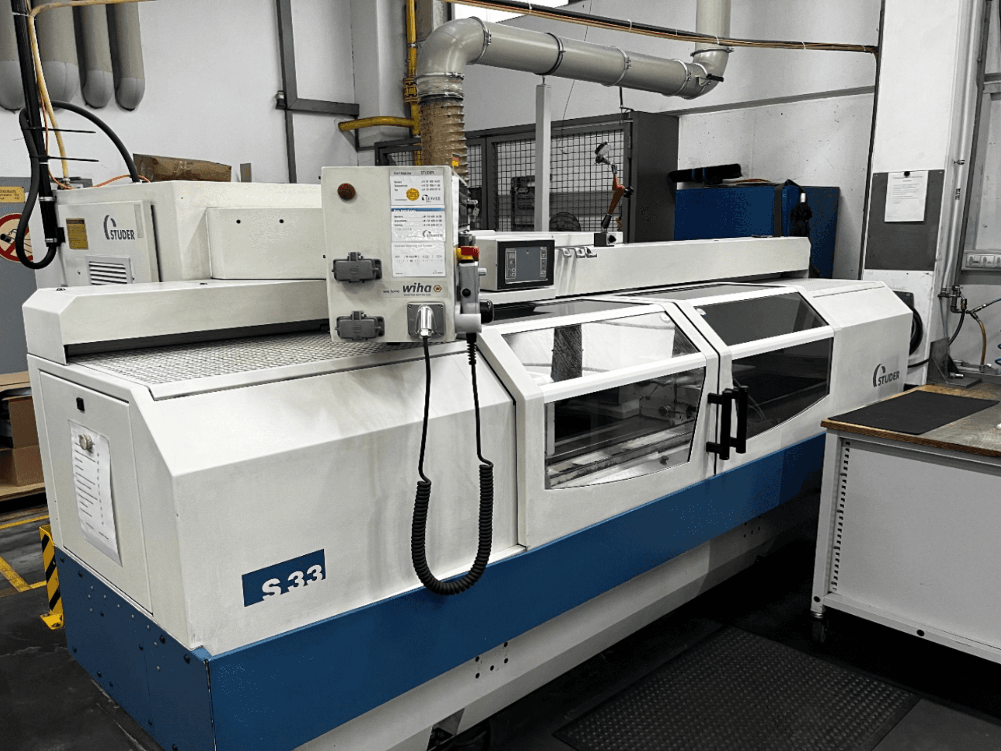 CNC bruska na kulato STUDER S33, pohled zepředu; ovládací panel a skleněné bezpečnostní dveře. Průmyslové prostředí.