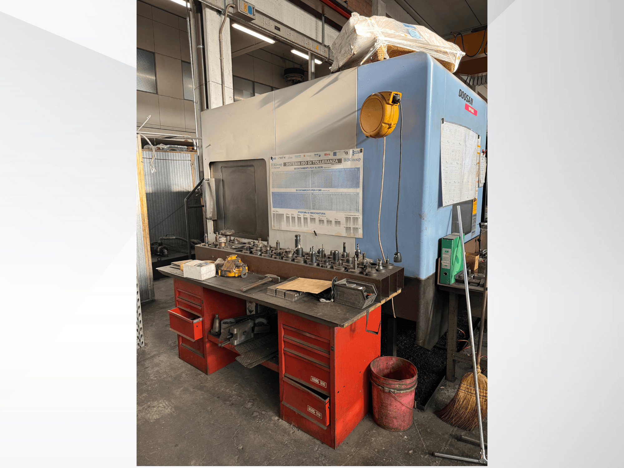 Obráběcí centrum Doosan s červeným pracovním stolem a úložným prostorem, na kterém jsou vystaveny nástroje a zařízení, pohled zepředu.