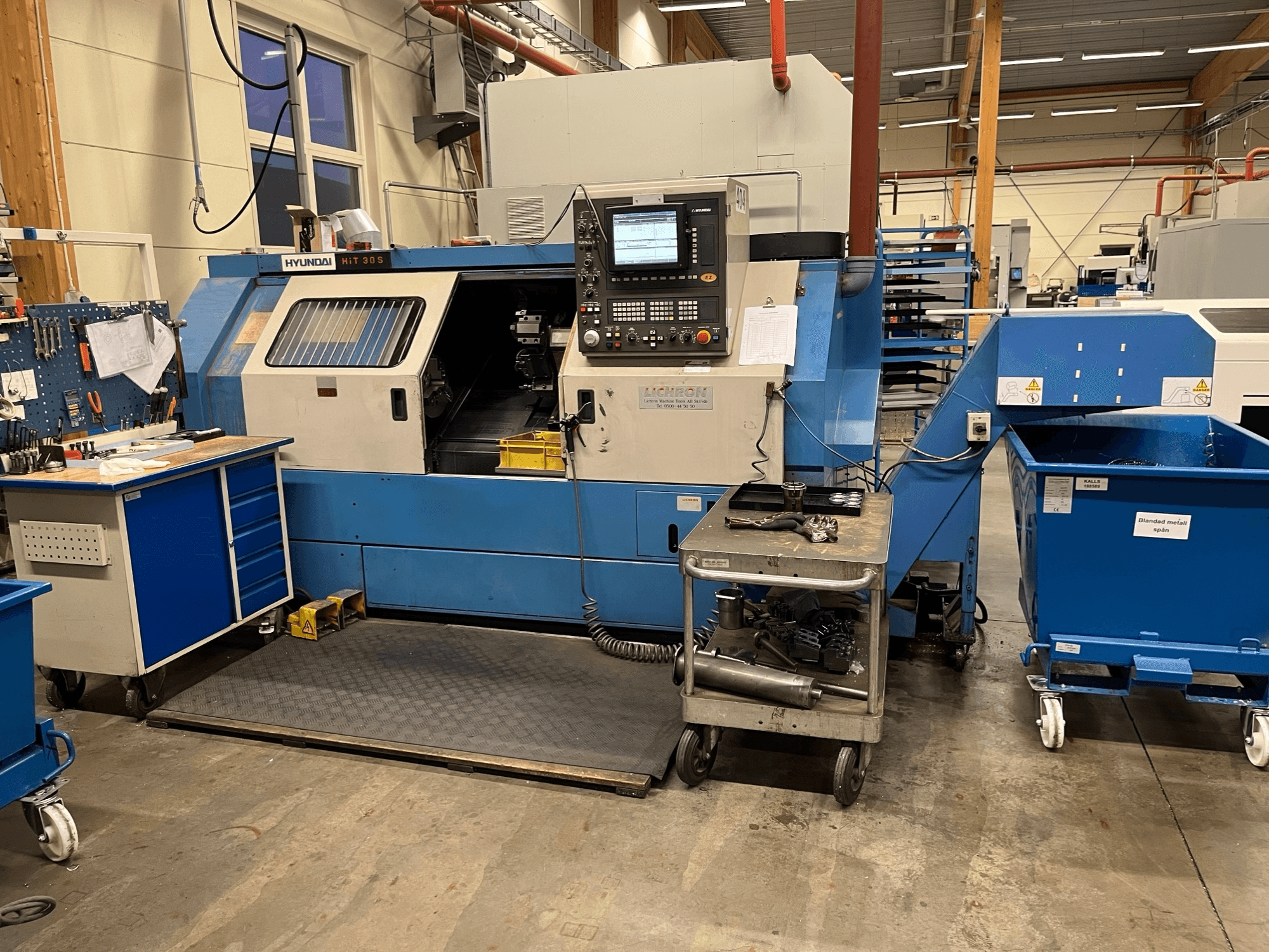 Horizontální soustruh Hyundai HIT 30S, pohled zepředu, s ovládacím panelem a nářadím na blízkém vozíku v dílně.