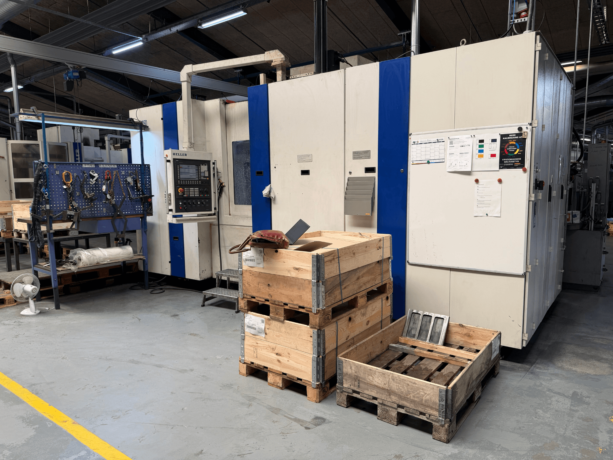 HORIZONTÁLNÍ OBRÁBĚCÍ CENTRUM HELLER MCH 250 v dílně, boční pohled s viditelnými dřevěnými paletami a stojanem na nářadí.