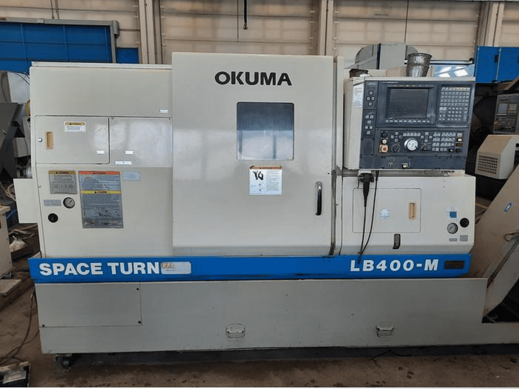 CNC soustruh Okuma LB400-M, čelní pohled s ovládacím panelem, výstražnými štítky a viditelným modrým nápisem "SPACE TURN".