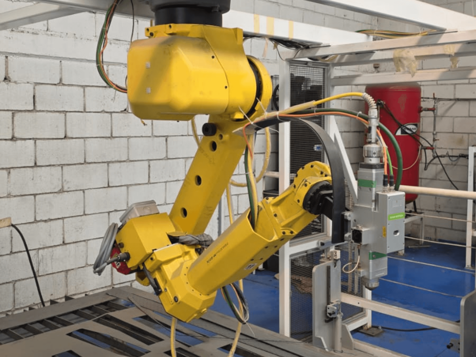 Žluté robotické rameno s přesným nástrojem s několika klouby a kabely, pohled zepředu v průmyslovém prostředí.