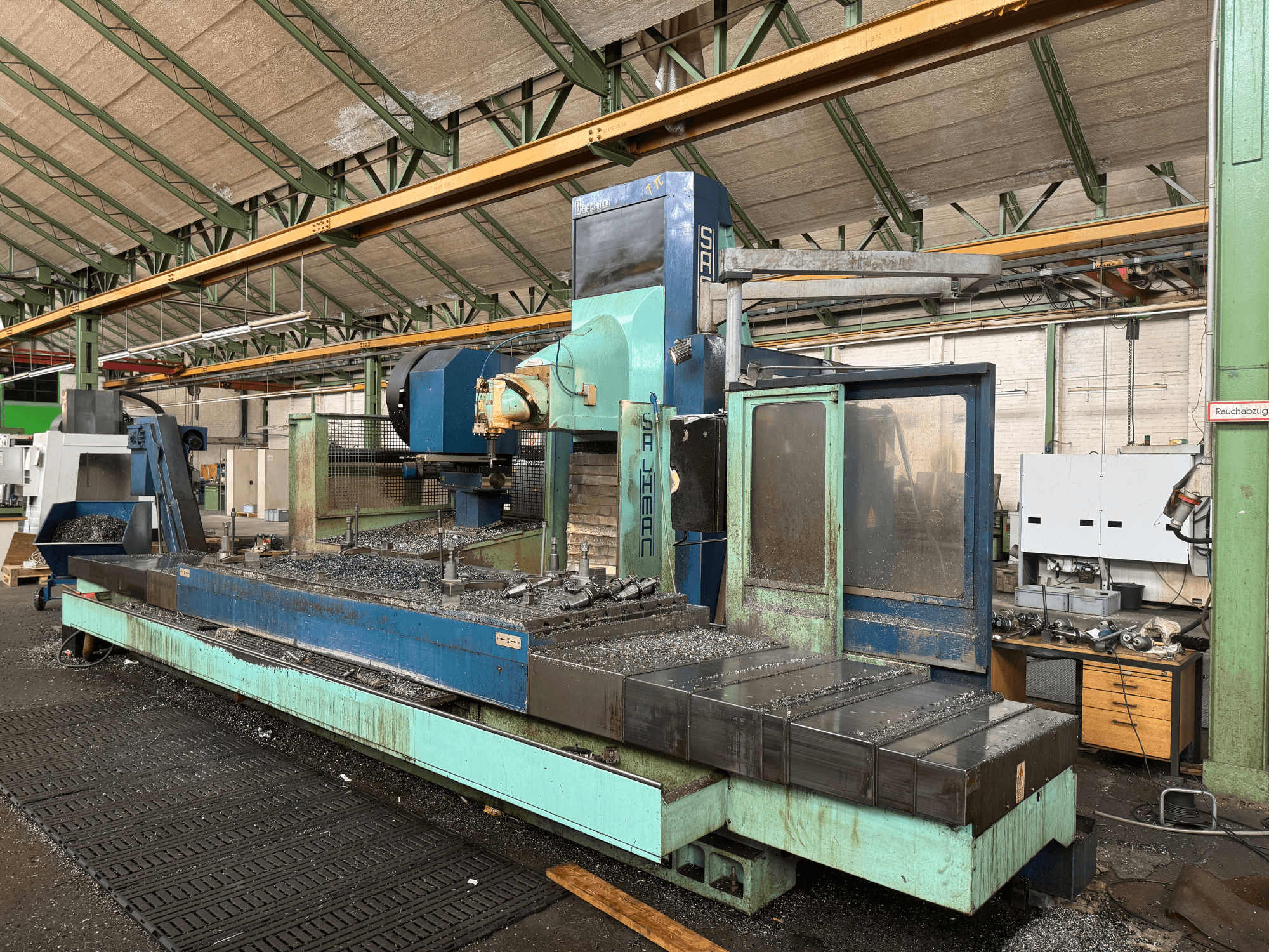 Frézka Salvador v továrním nastavení, pohled zepředu, modrá a zelená barva, na lůžku jsou vidět kovové hobliny.