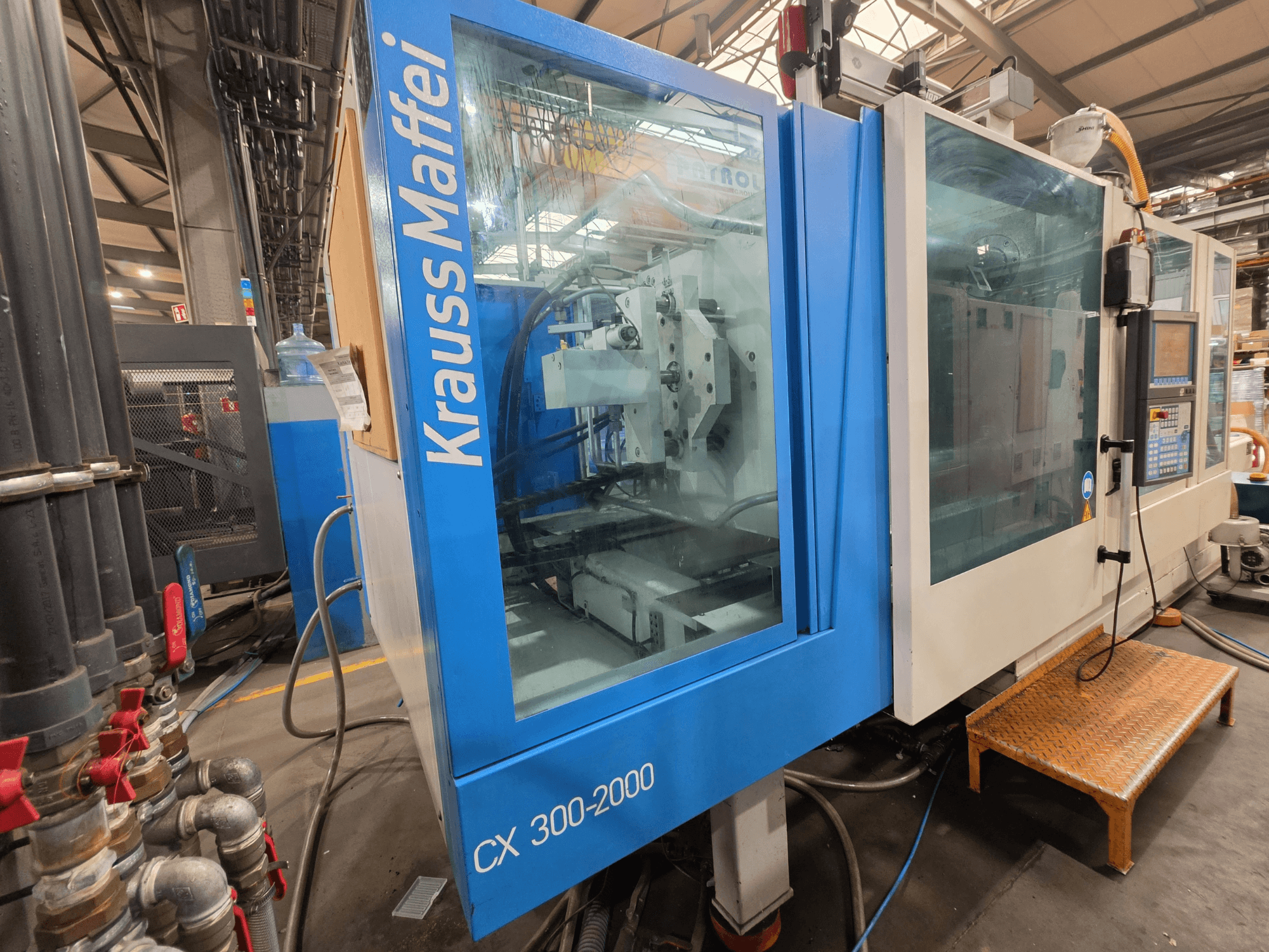 Hydraulický vstřikovací stroj Krauss Maffei CX 300-2000, pohled zepředu, ukazuje ovládací panel a hydraulické vedení.