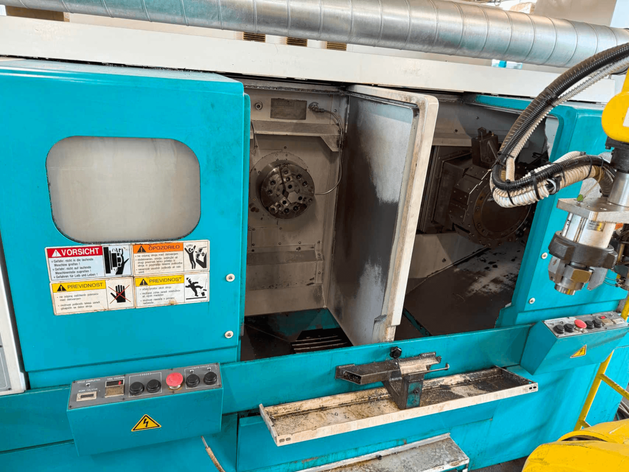 Horizontální soustruh DOOSAN H310T, pohled zepředu na ovládací panel a prostor vřetena s bezpečnostními upozorněními.