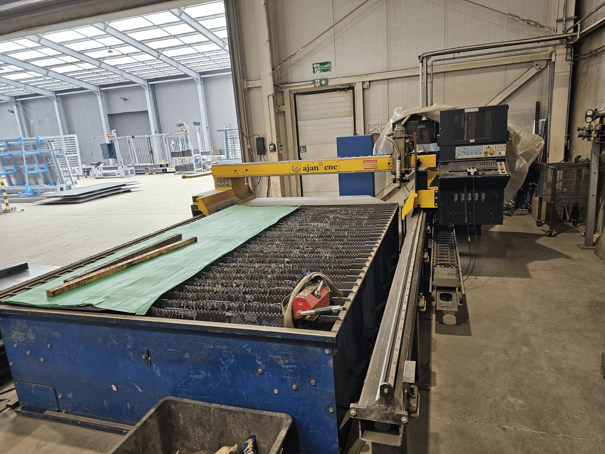 Automatický plazmový řezací stroj AJAN PP16011 v bočním pohledu, s řezacím stolem a ovládacím panelem, zasazený do dílenského prostředí.