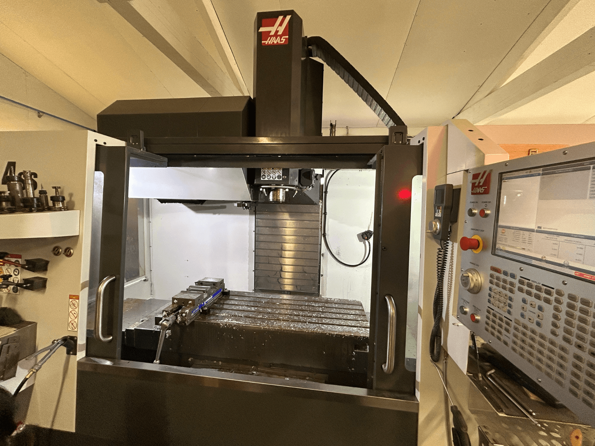Vertikální obráběcí centrum HAAS VF-4SS, pohled zepředu, ovládací panel, držák nástrojů a pracovní plocha s kovovými hoblinami.