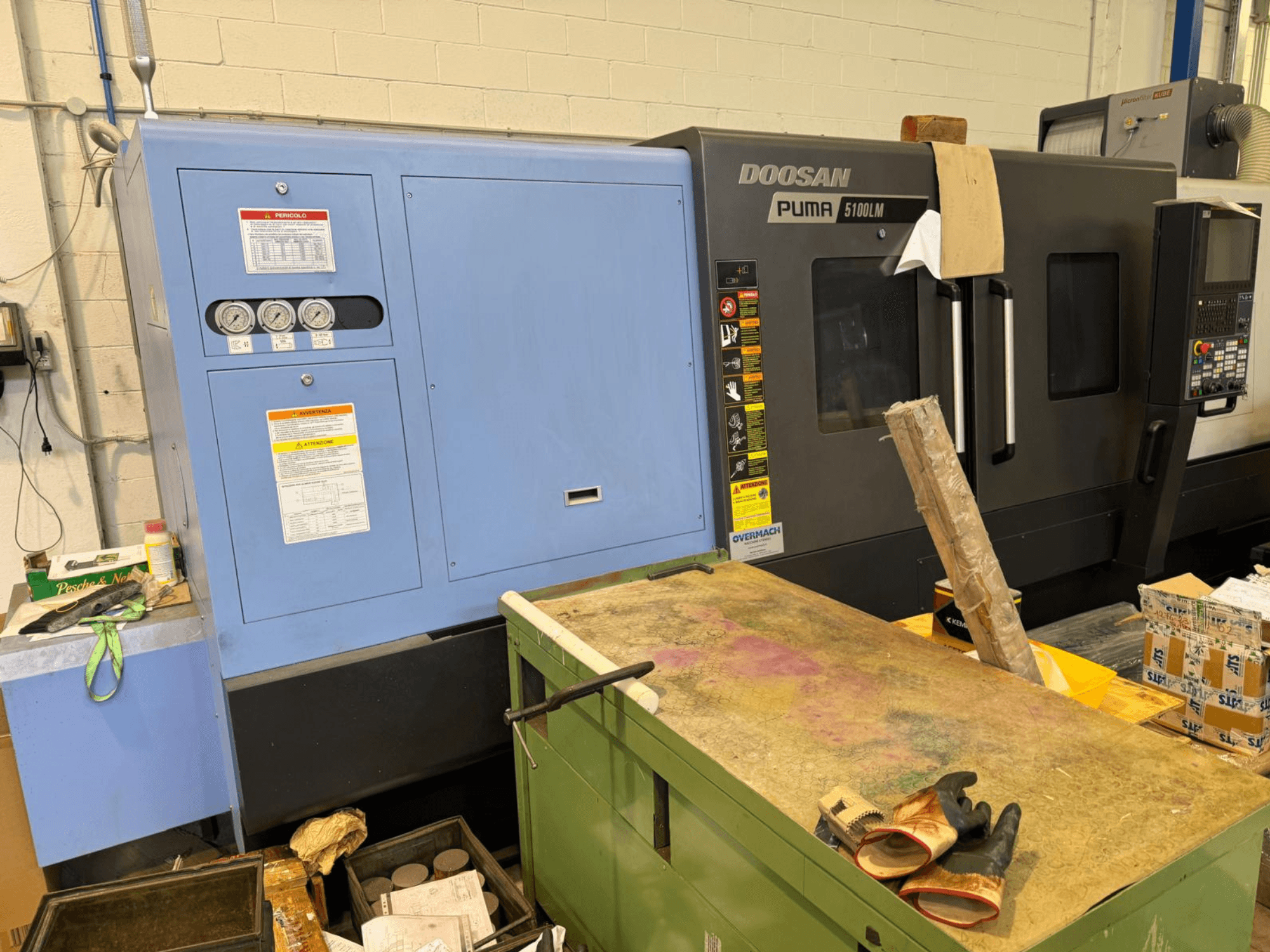 CNC stroj Doosan Puma 5100LM a ovládací panel, boční pohled. Na modré řídicí jednotce jsou viditelné ukazatele a výstražné štítky.