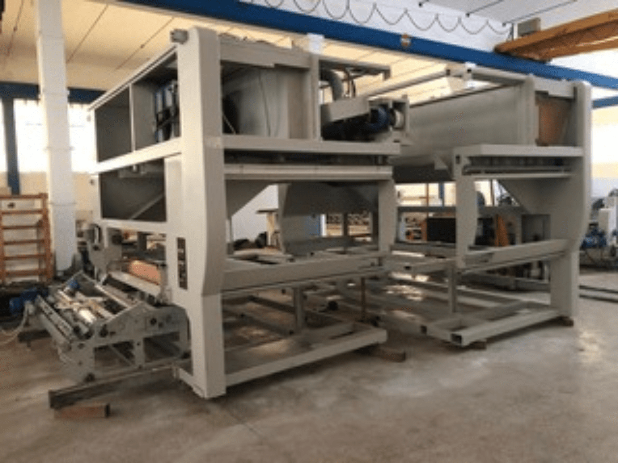 Průmyslový stroj s několika dopravními válečky a velkou konstrukcí; boční pohled, šedá barva, umístěný v dobře osvětlené továrně.