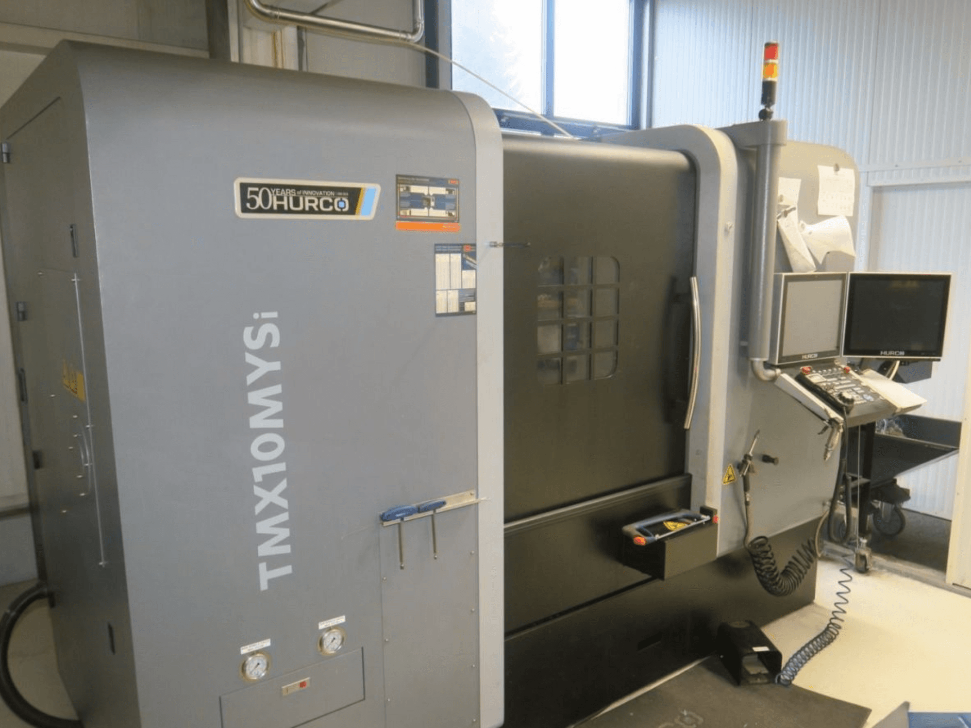 CNC stroj Hurco TMX10MYSi v bočním pohledu; zobrazený ovládací panel, nouzová světla a měřidla.